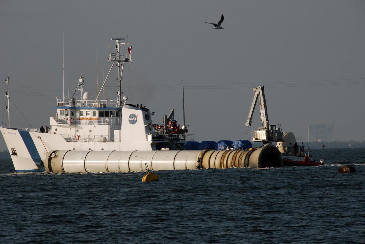 KENNEDY SPACE CENTER, FLA. --  The Freedom Star, one of NASA's solid rocket booster retrieval ships, tows a solid rocket booster alongside, heading for Hangar AF at Cape Canaveral Air Force Station.  Barely visible in the background at right is the Vehicle Assembly Building at NASA's Kennedy Space Center. The booster is from space shuttle Endeavour, which launched the STS-123 mission on March 11. The space shuttle’s solid rocket booster casings and associated flight hardware are recovered at sea. The boosters impact the Atlantic Ocean approximately seven minutes after liftoff. The splashdown area is a square of about 6 by 9 nautical miles located about 140 nautical miles downrange from the launch pad. The retrieval ships are stationed approximately 8 to 10 nautical miles from the impact area at the time of splashdown. As soon as the boosters enter the water, the ships accelerate to a speed of 15 knots and quickly close on the boosters, which they tow back to port.  After transfer to a position alongside the ship, the booster will be towed  to Hangar AF at Cape Canaveral Air Force Station. There, the expended boosters are disassembled, refurbished and reloaded with solid propellant for reuse.   Photo credit: NASA/Jack Pfaller