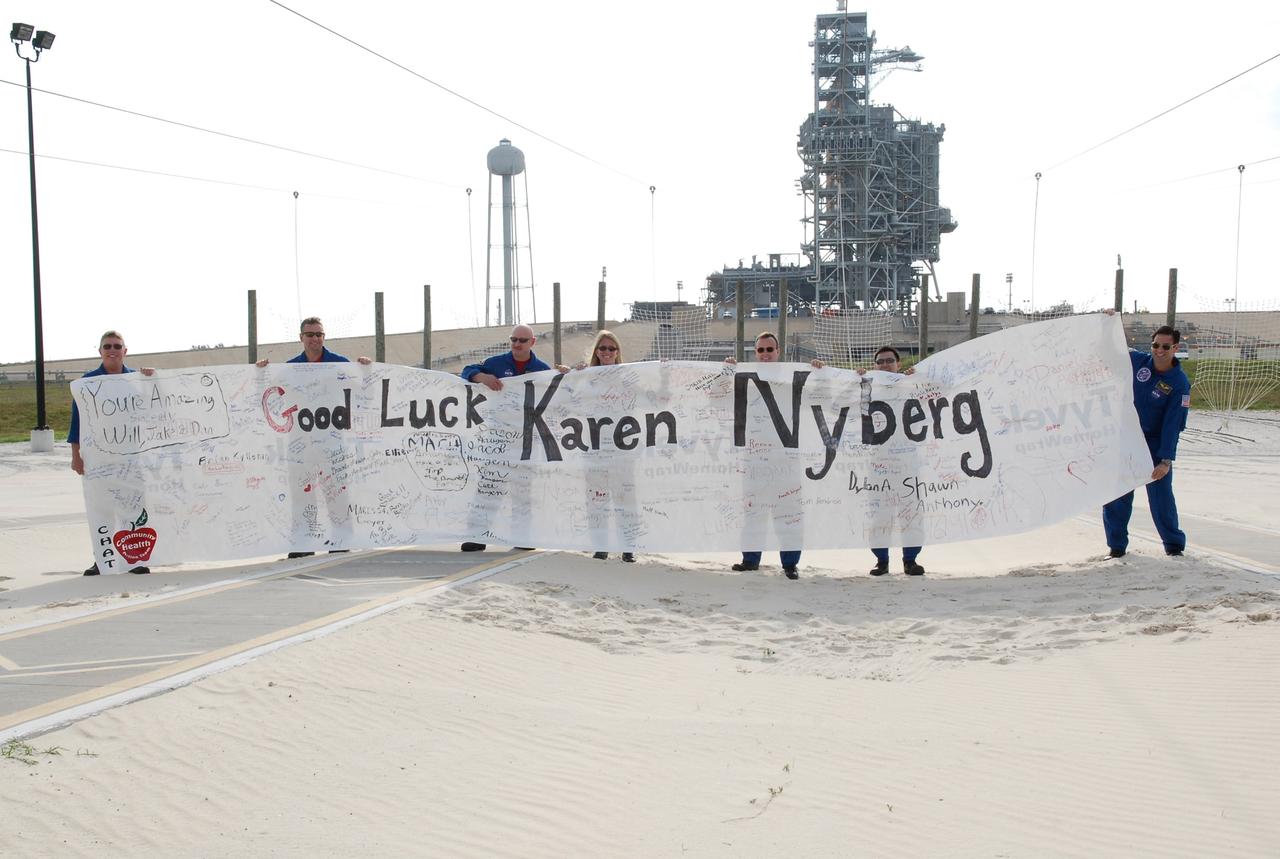 CAPE CANAVERAL, Fla. --  The STS-124 crew holds a good-luck banner presented to Mission Specialist Karen Nyberg that was created and signed by students at Henning Public School in the town of Henning, Minn.  Holding the banner are (from left) Mission Specialist Mike Fossum, Pilot Ken Ham, Commander Mark Kelly, Nyberg, Mission Specialists Ron Garan, Akihiko Hoshide and Greg Chamitoff.  Hoshide represents the Japan Aerospace Exploration Agency.  In the background is the 300-gallon water tower (left) and the fixed service structure.  The crew is at Kennedy for a dress launch rehearsal called the terminal countdown demonstration test. TCDT provides astronauts and ground crews with an opportunity to participate in various simulated countdown activities, including equipment familiarization and emergency training.  On the STS-124 mission, the crew will deliver and install the Japanese Experiment Module – Pressurized Module and Japanese Remote Manipulator System.  Discovery's launch is targeted for May 31.   Photo credit: NASA/Kim Shiflett