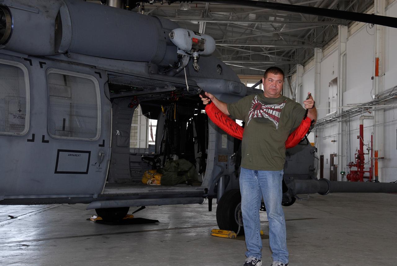 CAPE CANAVERAL, Fla. -- A representative of the 301st Rescue Squadron demonstrates rescue equipment that is used by participants in the Mode VIII exercise being conducted at Patrick Air Force Base, Fla. In the background is an HH-60G helicopter. In support of, and with logistical support from, NASA, USSTRATCOM is hosting a major exercise involving Department of Defense, Department of Homeland Security, search and rescue (SAR) forces, including the 45th Space Wing at Patrick Air Force Base, which support space shuttle astronaut bailout contingency operations, known as Mode VIII. This exercise tests SAR capabilities to locate, recover and provide medical treatment for astronauts following a space shuttle launch phase open-ocean bailout. Participants include members of the U.S. Navy, U.S. Coast Guard, U.S. Air Force, and NASA's Kennedy Space Center and Johnson Space Center. This will be the 15th Mode VIII exercise conducted in the past 20 years. Photo credit: NASA/Kim Shiflett