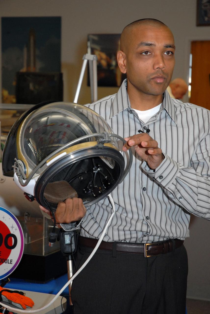 CAPE CANAVERAL, Fla. --  In the NASA News Center at NASA's Kennedy Space Center, Shuttle Crew Escape System Manager KC Chhipwadia describes for the media the elements of the helmet that is part of the launch and entry suit (seen on the table) used by shuttle crews during their missions.  He is holding onto the bar that latches to secure the closed visor.  The helmet provides oxygen when needed plus a communication system.   Photo credit:  NASA/Amanda Diller