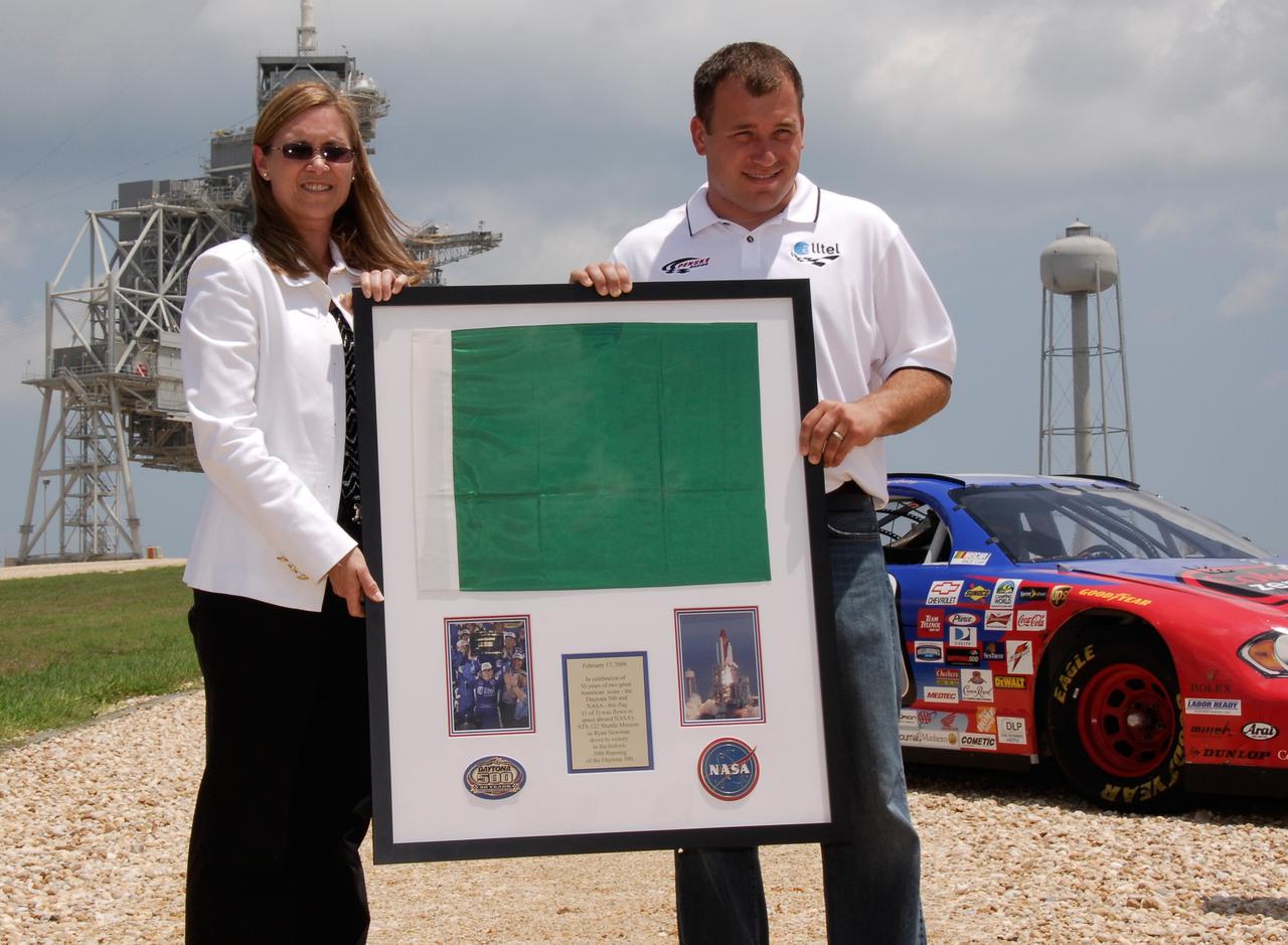 CAPE CANAVERAL, Fla.  –   On Launch Pad 39A at NASA's Kennedy Space Center, Janet Petro, Kennedy's deputy center director, presents 2008 Daytona 500 winner Ryan Newman one of the racing flags flown last February aboard space shuttle Atlantis' STS-122 mission to the International Space Station.  Behind him, at right, is the Daytona International Speedway show car.  Newman is visiting Kennedy in honor of NASA's 50th anniversary and the 50th running of NASCAR's Daytona 500 in February. NASA presented Newman two green racing flags.  One flag was given to Newman, the second was presented to Daytona 500 Experience General Manager Kim Isemann.  A third flag that was flown will be kept by NASA for public display.  The connection between NASA and Daytona's International Speedway extends beyond their close proximity to one another. During recent years, technology developed for the space program has found many uses on Earth, including helping NASCAR drivers stay safe and increase performance.  Photo credit: NASA/Kim Shiflett