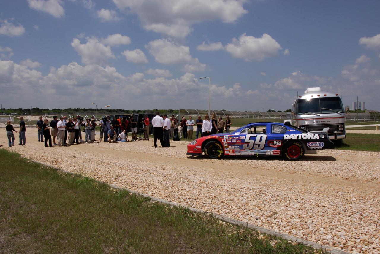 CAPE CANAVERAL, Fla.  –   Members of the media stretch across the crawlerway on Launch Pad 39A at NASA's Kennedy Space Center to interview 2008 Daytona 500 winner Ryan Newman (center right). At left is Daytona International Speedway President Robin Braig.  The Daytona International Speedway show car, shown here, is in sharp contrast to the crawler-transporter that usually travels the special road to the pad at a maximum speed of 2 mph. Newman is visiting Kennedy in honor of NASA's 50th anniversary and the 50th running of NASCAR's Daytona 500 in February. NASA presented Newman two green racing flags that were flown last February aboard space shuttle Atlantis' STS-122 mission to the International Space Station. One flag was given to Newman, the second was presented to Daytona 500 Experience General Manager Kim Isemann. A third flag that was flown will be kept by NASA for public display.  The connection between NASA and Daytona's International Speedway extends beyond their close proximity to one another. During recent years, technology developed for the space program has found many uses on Earth, including helping NASCAR drivers stay safe and increase performance.  Photo credit: NASA/Kim Shiflett