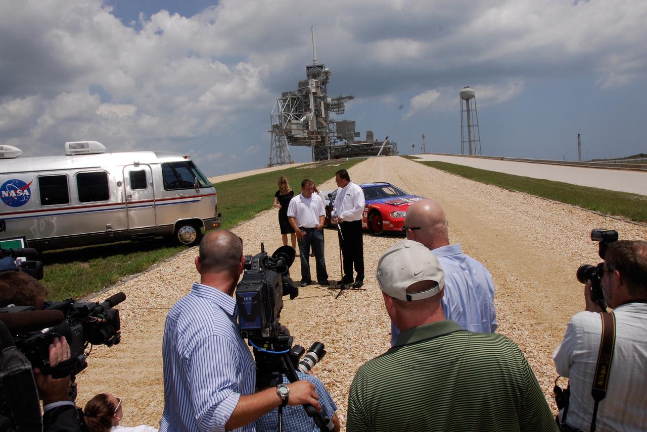 CAPE CANAVERAL, Fla.  –   2008 Daytona 500 winner Ryan Newman (left) and Daytona International Speedway President Robin Braig talk to the media gathered on the crawlerway on Launch Pad 39A at NASA's Kennedy Space Center.  The Daytona International Speedway show car, shown here, is in sharp contrast to the crawler-transporter that usually travels the special road to the pad.  Newman is visiting Kennedy in honor of NASA's 50th anniversary and the 50th running of NASCAR's Daytona 500 in February. NASA presented Newman two green racing flags that were flown last February aboard space shuttle Atlantis' STS-122 mission to the International Space Station. One flag was given to Newman, the second was presented to Daytona 500 Experience General Manager Kim Isemann. A third flag that was flown will be kept by NASA for public display.  The connection between NASA and Daytona's International Speedway extends beyond their close proximity to one another. During recent years, technology developed for the space program has found many uses on Earth, including helping NASCAR drivers stay safe and increase performance.  Photo credit: NASA/Kim Shiflett