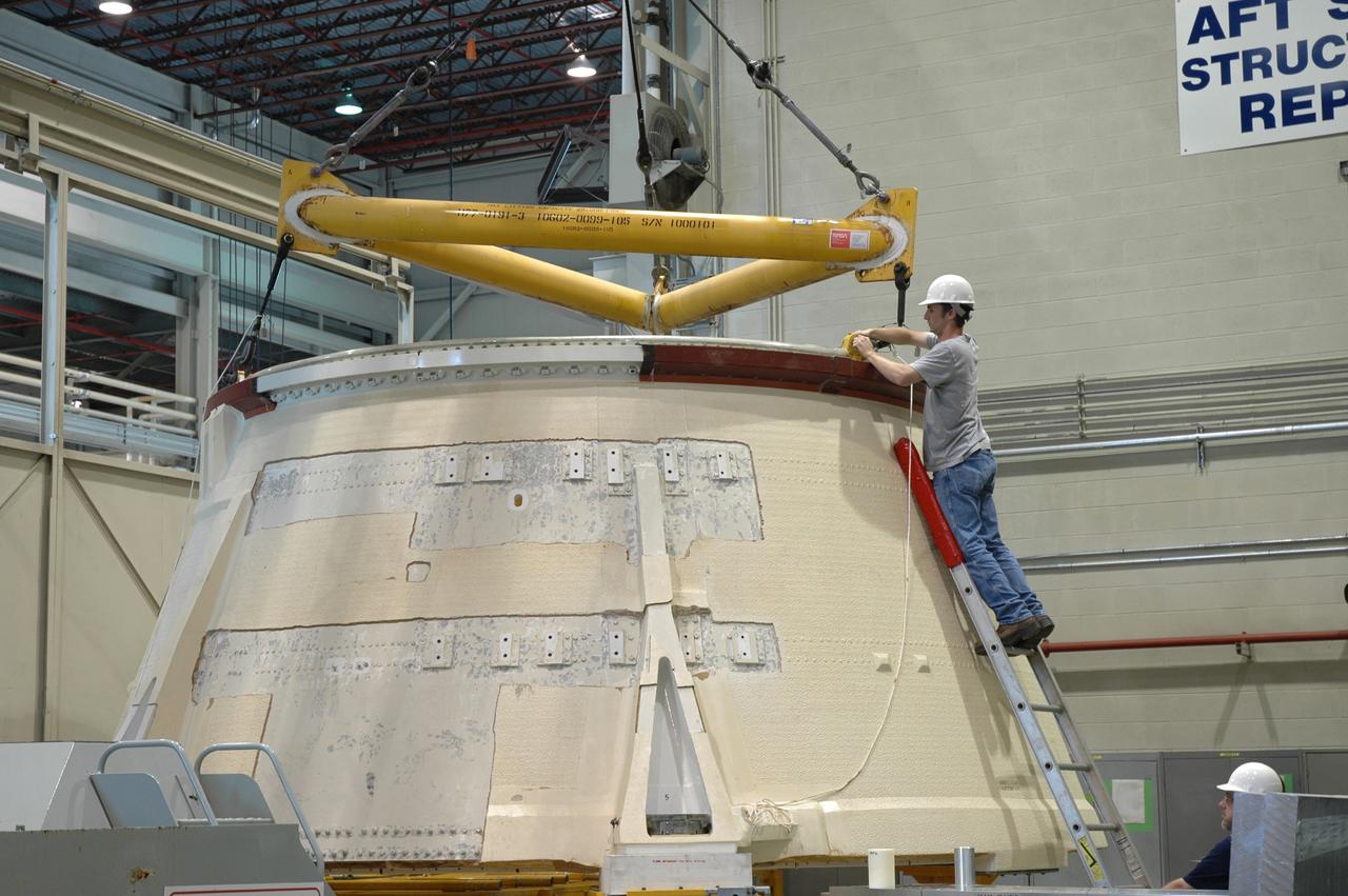 CAPE CANAVERAL, Fla.  –   In the Assembly and Refurbishment Facility at NASA's Kennedy Space Center, a worker attaches an overhead crane to the aft skirt for the Ares 1-X rocket.  The segment is being lifted into a machine shop work stand for drilling modifications.  The modifications will prepare it for the installation of the auxiliary power unit controller, the reduced-rate gyro unit, the booster decelerator motors and the booster tumble motors.  Ares I is an in-line, two-stage rocket that will transport the Orion crew exploration vehicle to low-Earth orbit.  Ares I-X is a test rocket. The Ares I first stage will be a five-segment solid rocket booster based on the four-segment design used for the shuttle.  Ares I’s fifth booster segment allows the launch vehicle to lift more weight and reach a higher altitude before the first stage separates from the upper stage, which ignites in midflight to propel the Orion spacecraft to Earth orbit.  Photo credit: NASA/Jim Grossmann