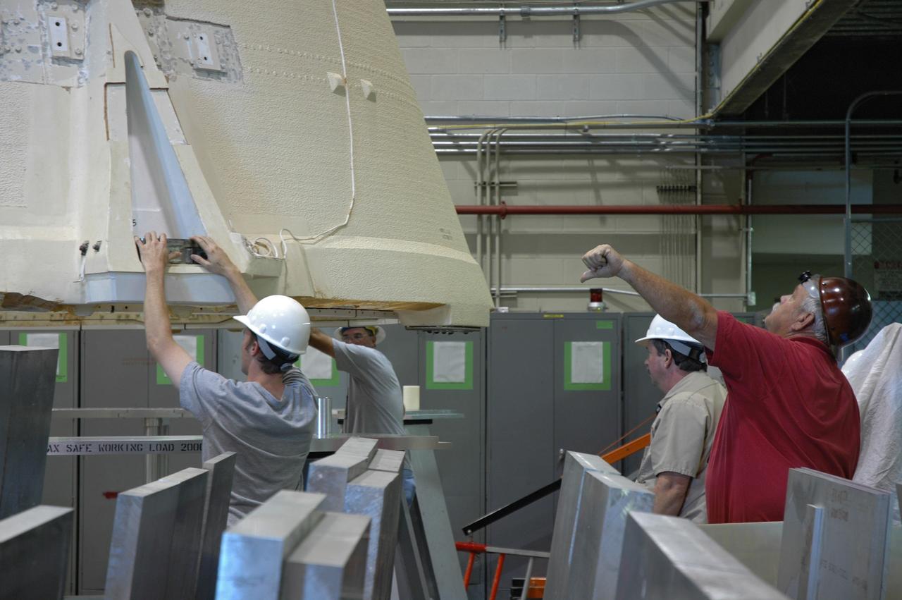 CAPE CANAVERAL, Fla.  –  In the Assembly and Refurbishment Facility at NASA's Kennedy Space Center, workers help guide the aft skirt for the Ares 1-X rocket as it is moved. The segment is being lifted into a machine shop work stand for drilling modifications.  The modifications will prepare it for the installation of the auxiliary power unit controller, the reduced-rate gyro unit, the booster decelerator motors and the booster tumble motors.  Ares I is an in-line, two-stage rocket that will transport the Orion crew exploration vehicle to low-Earth orbit.  Ares I-X is a test rocket. The Ares I first stage will be a five-segment solid rocket booster based on the four-segment design used for the shuttle.  Ares I’s fifth booster segment allows the launch vehicle to lift more weight and reach a higher altitude before the first stage separates from the upper stage, which ignites in midflight to propel the Orion spacecraft to Earth orbit.  Photo credit: NASA/Jim Grossmann