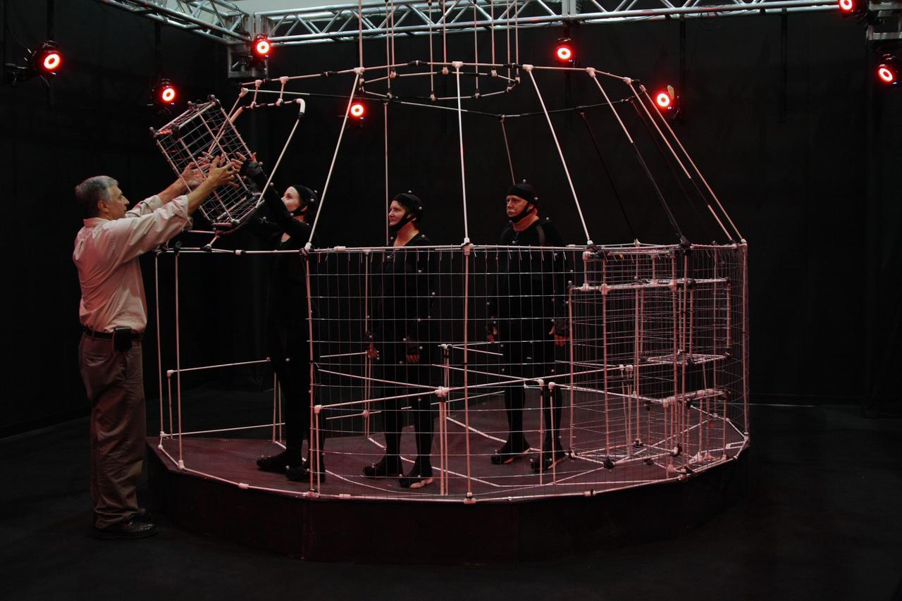 CAPE CANAVERAL, Fla. – Professor Peter Voci, NYIT MOCAP (Motion Capture) team director, (left) hands a component of the Orion Crew Module mockup to one of three technicians inside the mockup. The technicians wear motion capture suits. The motion tracking aims to improve efficiency of assembly processes and identify potential ergonomic risks for technicians assembling the mockup. The work is being performed in United Space Alliance's Human Engineering Modeling and Performance Lab in the RLV Hangar at NASA's Kennedy Space Center.  The motion tracking aims to improve efficiency of assembly processes and identify potential ergonomic risks for technicians assembling the mockup. The work is being performed in United Space Alliance's Human Engineering Modeling and Performance Lab in the RLV Hangar at NASA's Kennedy Space Center. Part of NASA's Constellation Program, the Orion spacecraft will return humans to the moon and prepare for future voyages to Mars and other destinations in our solar system.
