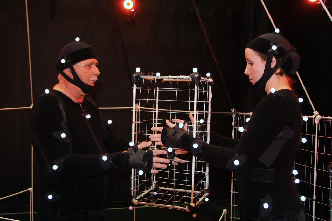 CAPE CANAVERAL, Fla. – A United Space Alliance technician (right) hands off a component of the Orion Crew Module mockup to one of the other technicians inside the mockup. The technicians wear motion capture suits. The motion tracking aims to improve efficiency of assembly processes and identify potential ergonomic risks for technicians assembling the mockup, which was created and built at the New York Institute of Technology by a team led by Prof. Peter Voci, MFA Director at the College of Arts and Sciences.  The motion tracking aims to improve efficiency of assembly processes and identify potential ergonomic risks for technicians assembling the mockup. The work is being performed in United Space Alliance's Human Engineering Modeling and Performance Lab in the RLV Hangar at NASA's Kennedy Space Center. Part of NASA's Constellation Program, the Orion spacecraft will return humans to the moon and prepare for future voyages to Mars and other destinations in our solar system.