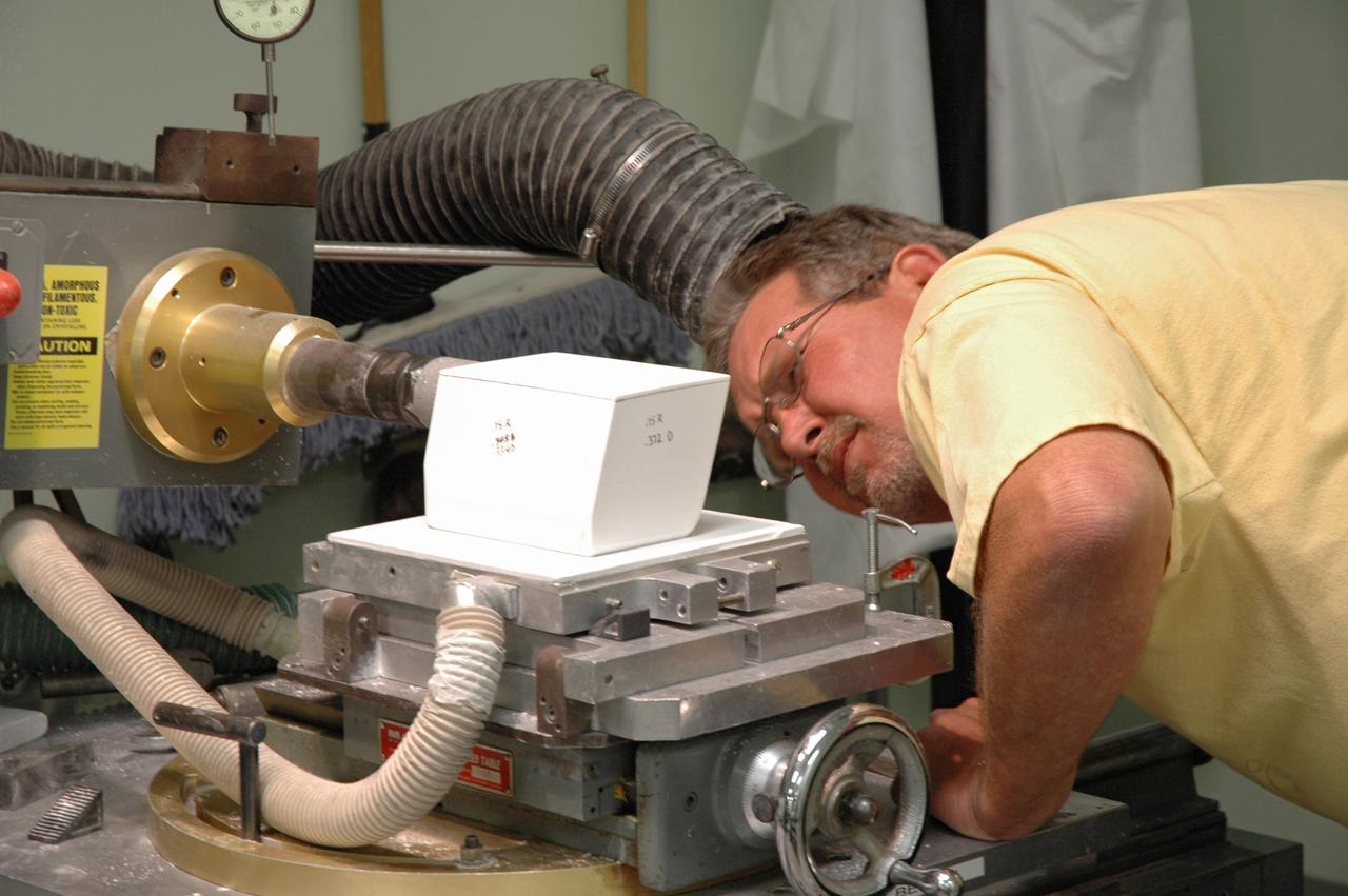 CAPE CANAVERAL, Fla. –   In the Tile Shop at NASA's Kennedy Space Center, a United Space Alliance technician checks the shape of Boeing Rigid Insulation-18, or BRI-18, tile he cut.  BRI-18 is the strongest material used for thermal insulation on the orbiters and, when coated to produce toughened unipiece fibrous insulation, provides a tile with extremely high-impact resistance.  It is replacing tiles on areas of the vehicle where impact risk is high.  These areas include the landing gear doors, the wing leading edge and the external tank doors.  Photo credit: NASA/Jim Grossmann
