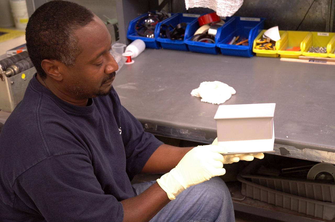 CAPE CANAVERAL, Fla. – In the tile shop at NASA's Kennedy Space Center, a worker holds one of the Boeing Replacement Insulation 18, or BRI-18, tiles being prepared for installation on space shuttles. BRI-18 is the strongest material used for thermal insulation on the orbiters and, when coated to produce toughened unipiece fibrous insulation, provides a tile with extremely high-impact resistance. It is replacing other tiles on areas of the vehicle where impact risk is high, such as the landing gear doors, the wing leading edge and the external tank doors. Photo credit: NASA/Jim Grossmann