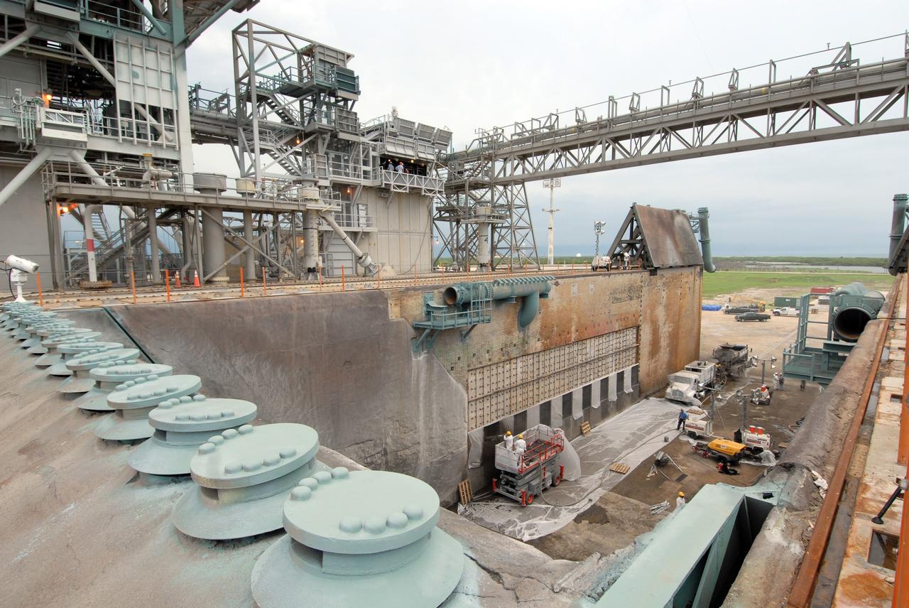 CAPE CANAVERAL, Fla. – This elevated view of Launch Pad 39A at NASA's Kennedy Space Center shows workers filling steel grid structures, welded to the wall of the flame trench, with a heat-resistant concrete called Fondue Fyre, developed during NASA's Apollo lunar program. At left are the pad's "rainbirds." These nozzles are part of the pad sound suppression system which protects the orbiter and its payloads from being damaged by acoustical energy reflected from the mobile launcher platform during liftoff. Damage to the trench occurred during the May 31 launch of Discovery on the STS-124 mission. A 75- by 20-foot section of the east wall was destroyed and debris scattered as far as the pad perimeter fence. Repairs are expected to be completed before the targeted Oct. 8 launch of Atlantis on the NASA Hubble Space Telescope servicing mission. Photo credit: NASA/Jack Pfaller