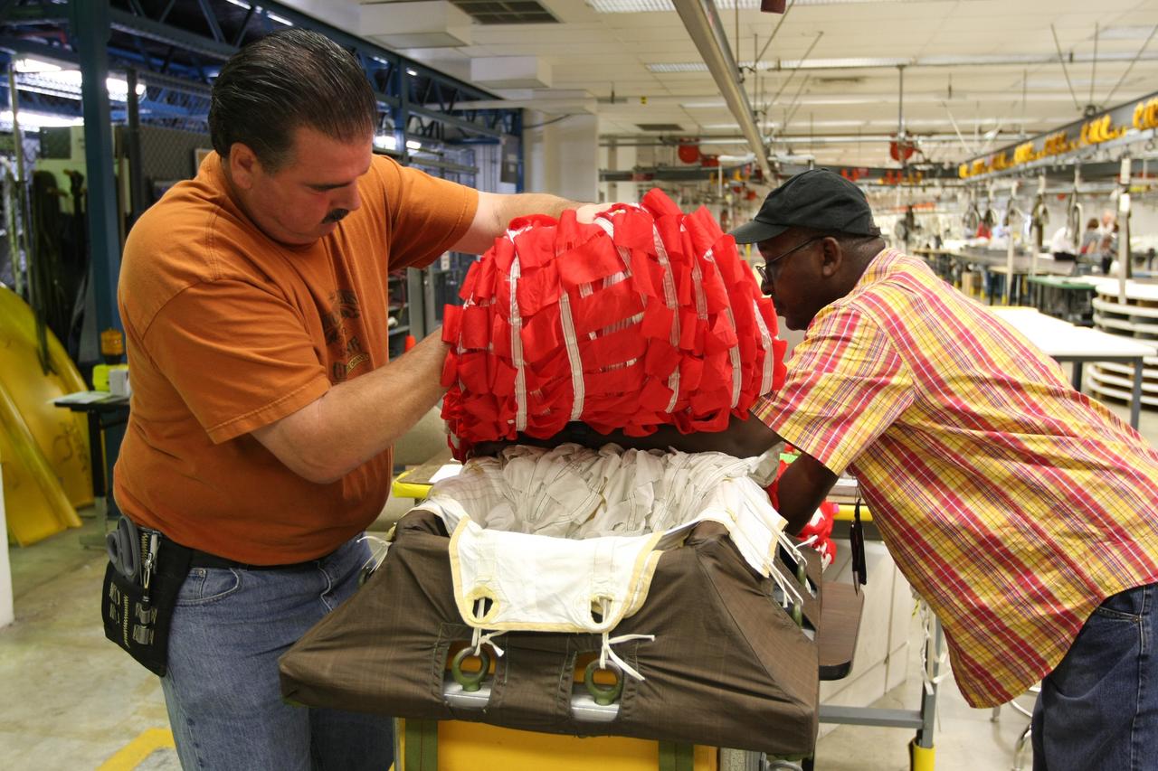 CAPE CANAVERAL, Fla. – In the Parachute Refurbishment Facility at NASA's Kennedy Space Center, technicians Mike Rothering (left) and James Murrell carefully fold an Ares-I parachute prior to packing. Ares I is an in-line, two-stage rocket that will transport the Orion crew exploration vehicle to low-Earth orbit. The Ares I first stage will be a five-segment solid rocket booster based on the four-segment design used for the shuttle. As with the shuttle, this booster will fall away when spent, lowered by parachute into the Atlantic Ocean where it can be retrieved for re-use. Photo credit: NASA/Dimitri Gerondidakis