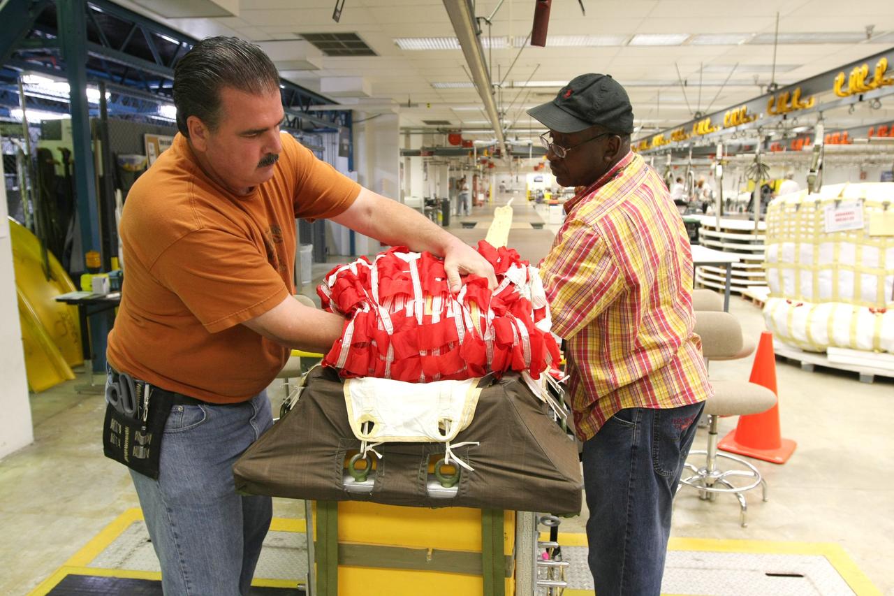 CAPE CANAVERAL, Fla. – In the Parachute Refurbishment Facility at NASA's Kennedy Space Center, technicians Mike Rothering (left) and James Murrell carefully fold an Ares-I parachute prior to packing. Ares I is an in-line, two-stage rocket that will transport the Orion crew exploration vehicle to low-Earth orbit. The Ares I first stage will be a five-segment solid rocket booster based on the four-segment design used for the shuttle. As with the shuttle, this booster will fall away when spent, lowered by parachute into the Atlantic Ocean where it can be retrieved for re-use. Photo credit: NASA/Dimitri Gerondidakis