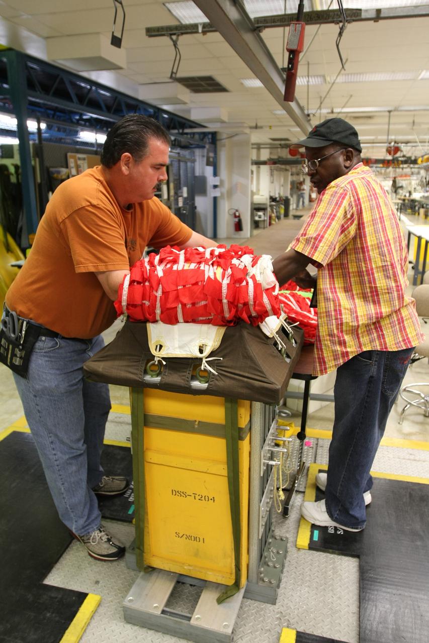 CAPE CANAVERAL, Fla. – In the Parachute Refurbishment Facility at NASA's Kennedy Space Center, technicians Mike Rothering (left) and James Murrell carefully fold an Ares-I parachute prior to packing. Ares I is an in-line, two-stage rocket that will transport the Orion crew exploration vehicle to low-Earth orbit. The Ares I first stage will be a five-segment solid rocket booster based on the four-segment design used for the shuttle. As with the shuttle, this booster will fall away when spent, lowered by parachute into the Atlantic Ocean where it can be retrieved for re-use. Photo credit: NASA/Dimitri Gerondidakis