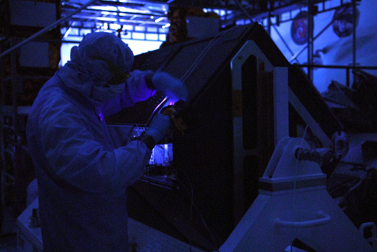 CAPE CANAVERAL, Fla. – In the clean room of the Payload Hazardous Processing Facility at NASA's Kennedy Space Center, a worker from NASA's Goddard Space Flight Center uses black light inspection for a thorough cleaning of the Cosmic Origins Spectrograph, or COS. Black light inspection uses UVA fluorescence to detect possible particulate microcontamination, minute cracks or fluid leaks. The COS will be installed on the Hubble Space Telescope on space shuttle Atlantis' STS-125 mission. COS will be the most sensitive ultraviolet spectrograph ever flown on Hubble and will probe the "cosmic web" - the large-scale structure of the universe whose form is determined by the gravity of dark matter and is traced by galaxies and intergalactic gas. The COS far-ultraviolet channel has a sensitivity 30 times greater than that of previous spectroscopic instruments for the detection of extremely low light levels. Launch of Atlantis on the STS-125 mission is targeted for Oct. 8. Photo credit: NASA/Kim Shiflett