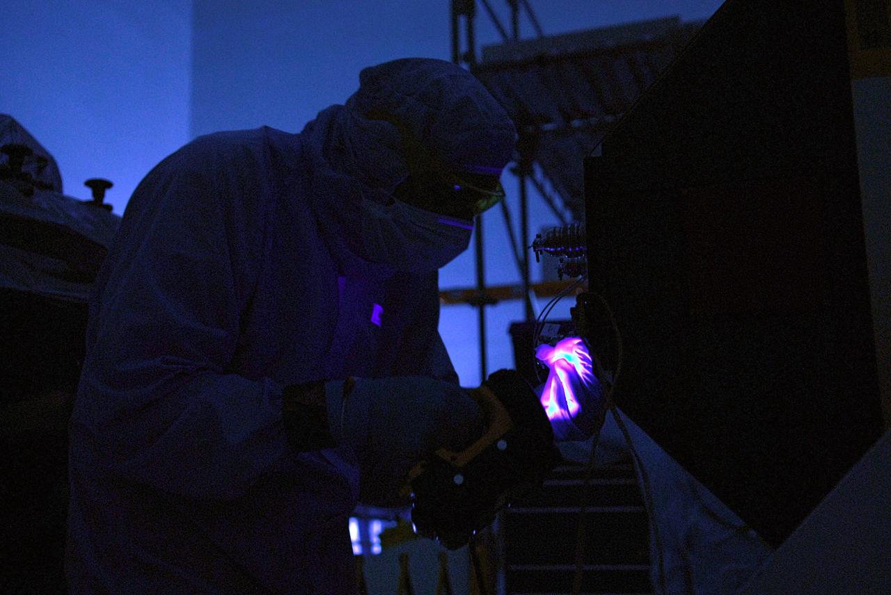 CAPE CANAVERAL, Fla. – In the clean room of the Payload Hazardous Processing Facility at NASA's Kennedy Space Center, a worker from NASA's Goddard Space Flight Center uses black light inspection for a thorough cleaning of the Cosmic Origins Spectrograph, or COS.  Black light inspection uses UVA fluorescence to detect possible particulate microcontamination, minute cracks or fluid leaks. The COS will be installed on the Hubble Space Telescope on space shuttle Atlantis' STS-125 mission. COS will be the most sensitive ultraviolet spectrograph ever flown on Hubble and will probe the "cosmic web" - the large-scale structure of the universe whose form is determined by the gravity of dark matter and is traced by galaxies and intergalactic gas. The COS far-ultraviolet channel has a sensitivity 30 times greater than that of previous spectroscopic instruments for the detection of extremely low light levels. Launch of Atlantis on the STS-125 mission is targeted for Oct. 8. Photo credit: NASA/Kim Shiflett