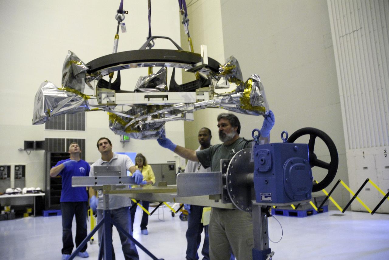 CAPE CANAVERAL, Fla. – In the Payload Hazardous Servicing Facility at NASA's Kennedy Space Center, a technician stabilizes the Soft Capture Mechanism (SCM), part of the Soft Capture and Rendezvous System, or SCRS, as it is lowered onto a stand. The SCRS will enable the future rendezvous, capture and safe disposal of Hubble by either a crewed or robotic mission. The ring-like device attaches to Hubble’s aft bulkhead. The SCRS greatly increases the current shuttle capture interfaces on Hubble, therefore significantly reducing the rendezvous and capture design complexities associated with the disposal mission. The SCRS comprises the Soft Capture Mechanism system and the Relative Navigation System and is part of the payload on the fifth and final Hubble servicing mission, STS-125, targeted for launch Oct. 8. Photo credit: NASA/Jack Pfaller