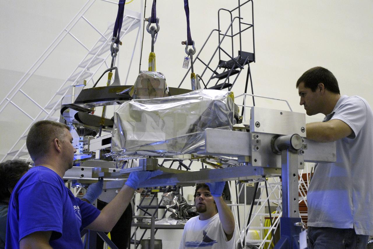 CAPE CANAVERAL, Fla. – In the Payload Hazardous Servicing Facility at NASA's Kennedy Space Center, technicians monitor the placement of the Soft Capture Mechanism (SCM), part of the Soft Capture and Rendezvous System, or SCRS, as it is lowered onto a stand. The SCRS will enable the future rendezvous, capture and safe disposal of Hubble by either a crewed or robotic mission. The ring-like device attaches to Hubble’s aft bulkhead. The SCRS greatly increases the current shuttle capture interfaces on Hubble, therefore significantly reducing the rendezvous and capture design complexities associated with the disposal mission. The SCRS comprises the Soft Capture Mechanism system and the Relative Navigation System and is part of the payload on the fifth and final Hubble servicing mission, STS-125, targeted for launch Oct. 8. Photo credit: NASA/Jack Pfaller