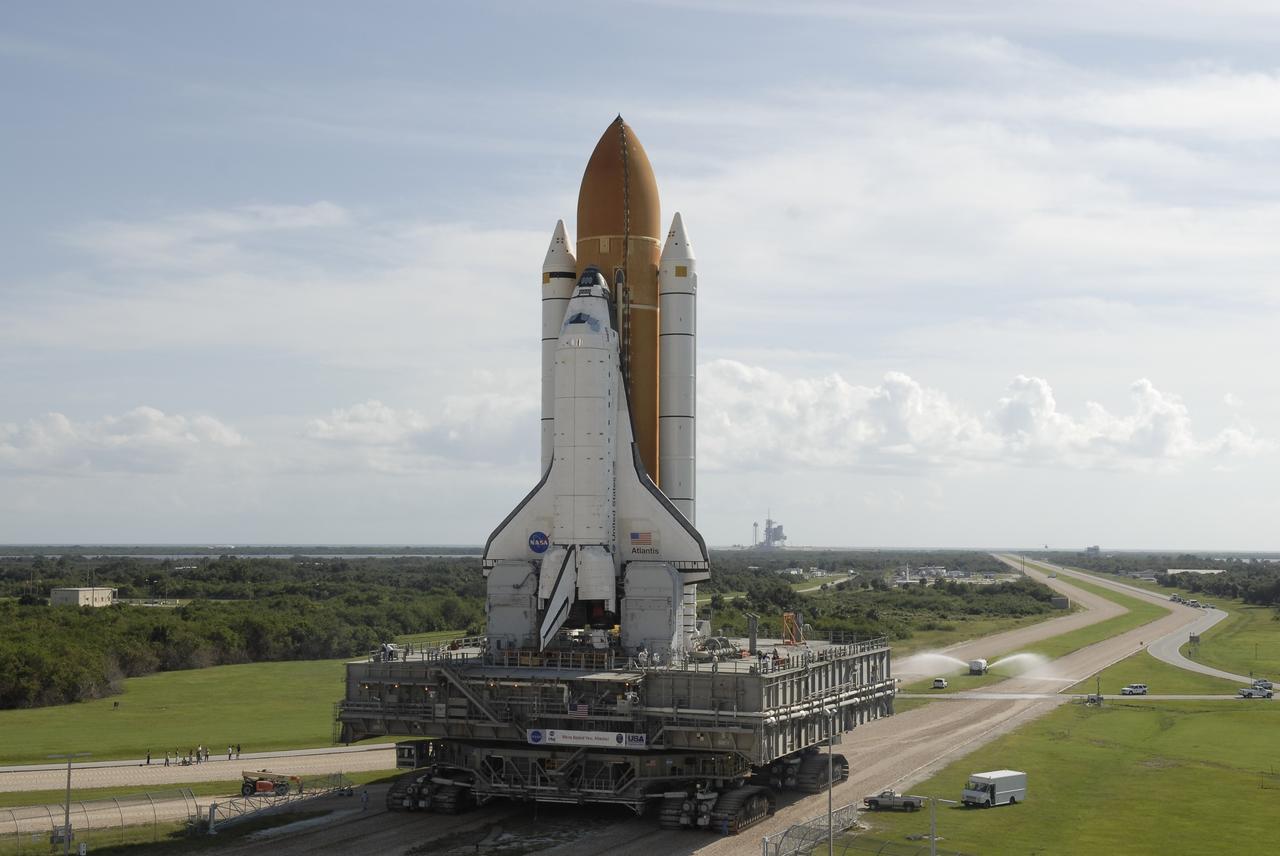 CAPE CANAVERAL, Fla. –  Space shuttle Atlantis rolls along the crawlerway toward Launch pad 39A, in the background, after leaving the Vehicle Assembly Building at NASA’s Kennedy Space Center.  A water truck sprays the crawlerway to minimize dust. The shuttle stack, with solid rocket boosters and external fuel tank attached to Atlantis, rest on the mobile launcher platform.  Movement is provided by the crawler-transporter underneath.  First motion occurred at 9:19 a.m. EDT. The Sept. 2 rollout date was postponed due to Tropical Storm Hanna’s shift to a northern track. Atlantis is scheduled to launch on the STS-125 mission to service NASA’s Hubble Space Telescope.  Launch is targeted for Oct. 8.  Photo credit: NASA/Kim Shiflett