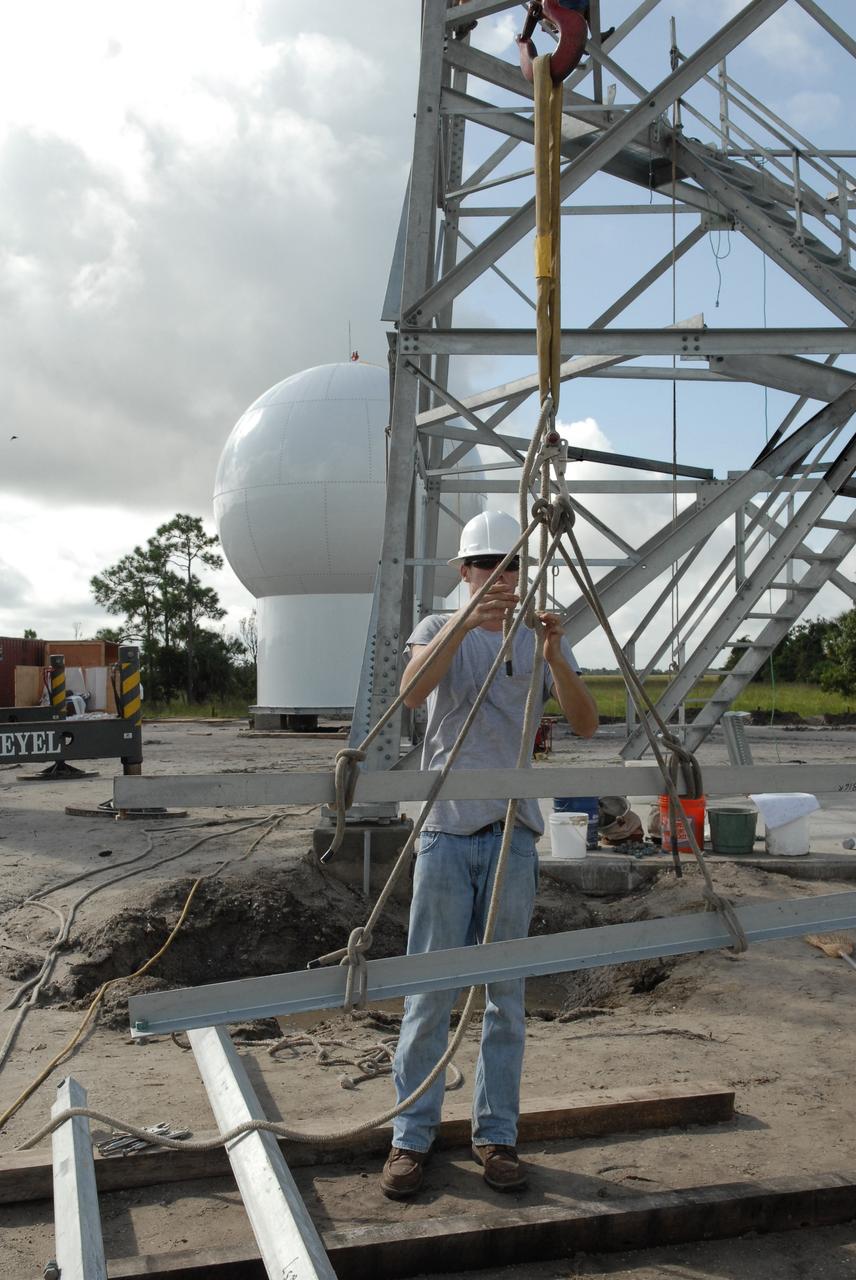 CAPE CANAVERAL, Fla. – In an area near S.R. 520 in Orange County, Florida, a worker finishes tying a line to a steel beam that will be added to a tower being constructed for a Doppler weather radar facility for the 45th Weather Squadron. In the background is the radome that will be on top of the tower. The new site replaces one at Patrick Air Force Base. It will be used by NASA's Kennedy Space Center, the 45th Space Wing and their customers. The site will be able to monitor weather conditions directly above and surrounding the launch pads at Kennedy.  The weather radar is essential in issuing lightning and other severe weather warnings and vital in evaluating lightning launch commit criteria.  The new radar, replacing what was installed 25 years ago at Patrick Air Force Base, includes Doppler capability to detect winds and identify the type, size and number of precipitation particles.  The site is ideally distant from the launch pads and has unobstructed views of Cape Canaveral Air Force Station and Kennedy. The radar will be used by forecasters at the USAF 45th Weather Squadron. Photo credit: NASA/Troy Cryder
