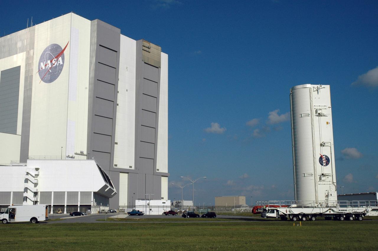 CAPE CANAVERAL, Fla. –    On NASA's Kennedy Space Center in Florida, the canister with space shuttle Atlantis’ HST payload inside rolls past the Vehicle Assembly Building and Launch Control Center, at left. The payload comprises four carriers holding various equipment for the mission.  The hardware will be transported back to Kennedy’s Payload Hazardous Servicing Facility where it will be stored until a new target launch date can be set for Atlantis’ STS-125 mission in 2009.  Atlantis’ October target launch date was delayed after a device on board Hubble used in the storage and transmission of science data to Earth shut down on Sept. 27.  Replacing the broken device will be added to Atlantis’ servicing mission to the telescope.  Photo credit: NASA/Jim Grossmann