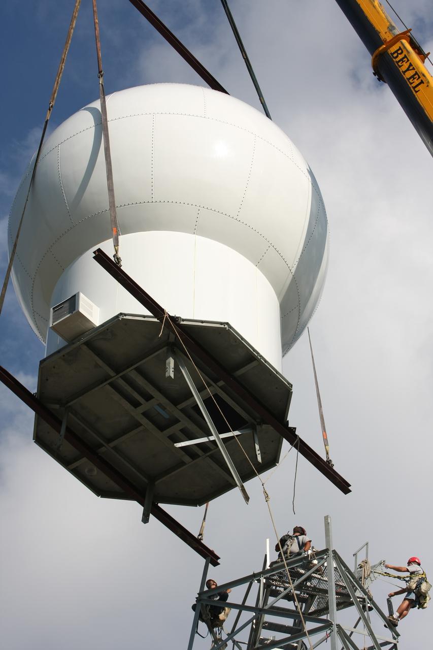 CAPE CANAVERAL, Fla. - Workers watch as the radome is delivered by crane to the top of a new Doppler weather radar tower being built in an area near S.R. 520 in Orange County, Fla. The dome houses the weather radar dish and pedestal and protects them from the elements.  The new tower will replace one at nearby Patrick Air Force Base and will be used by NASA's Kennedy Space Center, the 45th Space Wing and their customers. The tower will be able to monitor weather conditions directly above the launch pads at Kennedy. The weather radar is essential in issuing lightning and other severe weather warnings and vital in evaluating lightning launch commit criteria. The new radar, replacing what was installed 25 years ago, includes Doppler capability to detect winds and identify the type, size and number of precipitation particles. The site is ideally distant from the launch pads and has unobstructed views of Cape Canaveral Air Force Station and Kennedy. Photo credit: NASA/Dimitri Gerondidakis