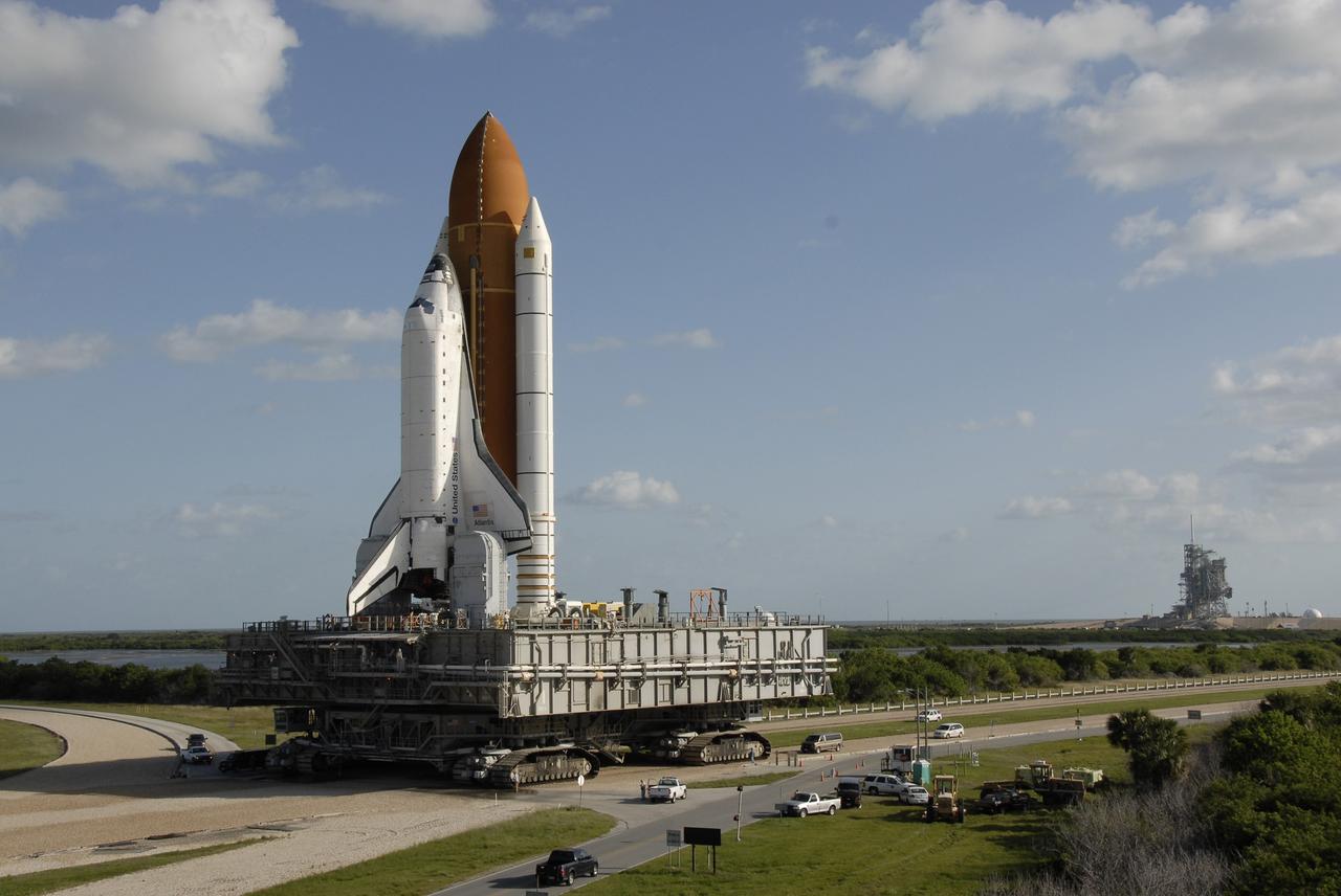 CAPE CANAVERAL, Fla. -    Space shuttle Atlantis rolls away from the rotating and fixed service structures (right) on  Launch Pad 39A at NASA's Kennedy Space Center in Florida. First motion was at 6:48 a.m. EDT. Atlantis sits on the mobile launcher platform, which in turn rests on the crawler-transporter, traveling less than 1 mph. Atlantis is rolling back to the Vehicle Assembly Building to await launch on its STS-125 mission to repair NASA's Hubble Space Telescope.  Atlantis' targeted launch on Oct. 14 was delayed when a system that transfers science data from the orbiting observatory to Earth malfunctioned on Sept. 27. The new target launch date is under review.  The space shuttle is mounted on a Mobile Launcher Platform and will be delivered to the Vehicle Assembly Building atop a crawler transporter. traveling slower than 1 mph during the 3.4-mile journey.  The rollback is expected to take approximately six hours.  Photo credit: NASA/Kim Shiflett
