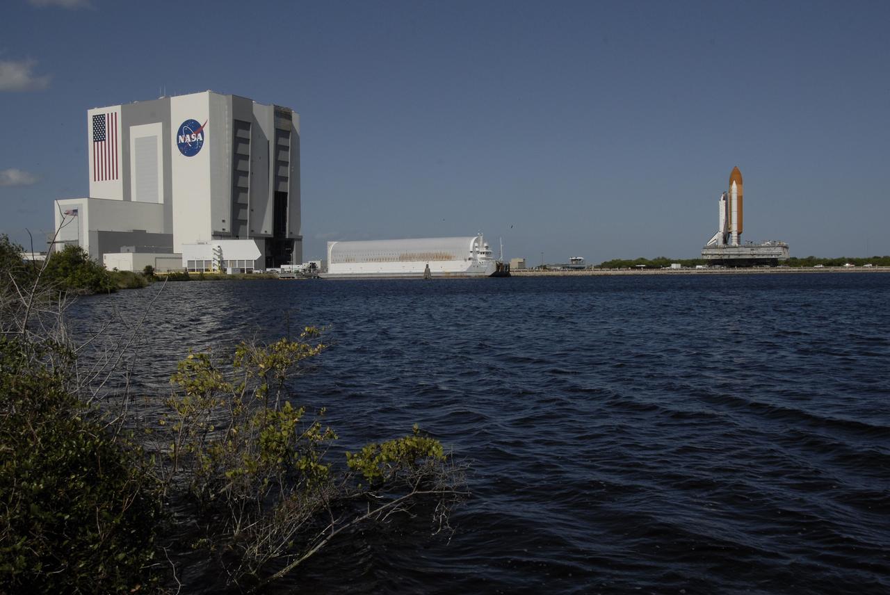 CAPE CANAVERAL, Fla. - Space shuttle Atlantis (right) rolls toward the Vehicle Assembly Building (far left) via the crawlerway at NASA's Kennedy Space Center in Florida after rolling back from Launch Pad 39A. In the VAB, Atlantis will await launch on its STS-125 mission to repair NASA's Hubble Space Telescope.  Between them is the Pegasus barge in the turn basin.  First motion of Atlantis off the pad was at 6:48 a.m. EDT. The journey was expected to take about six hours. Atlantis' targeted launch on Oct. 14 was delayed when a system that transfers science data from the orbiting observatory to Earth malfunctioned on Sept. 27. The new target launch date is under review.  Photo credit: NASA/Kim Shiflett