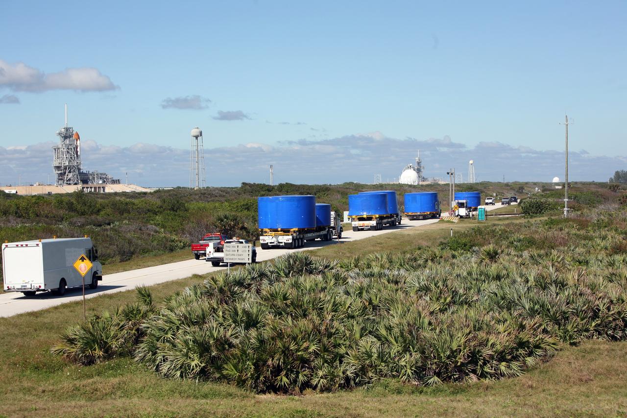 CAPE CANAVERAL, Fla. – A convoy of trucks passes a launch pad as it makes the journey from Port Canaveral, Fla., to the Vehicle Assembly Building's high bay 4 at NASA's Kennedy Space Center in Florida. The trucks carry Ares I-X upper stage simulator segments. The upper stage simulator will be used in the test flight identified as Ares I-X in 2009. The Ares I-X test flight will provide NASA an early opportunity to test and prove hardware, facilities and ground operations associated with the Ares I crew launch vehicle. It also will allow NASA to gather critical data during ascent of the integrated Orion crew exploration vehicle and the Ares I rocket. The data will ensure the entire vehicle system is safe and fully operational before astronauts begin traveling to orbit. The simulator segments will simulate the mass and the outer mold line and will be more than 100 feet of the total vehicle height of 327 feet. The simulator comprises 11 segments that are approximately 18 feet in diameter. Most of the segments will be approximately 10 feet high, ranging in weight from 18,000 to 60,000 pounds, for a total of approximately 450,000 pounds. Photo credit: NASA/Cory Huston