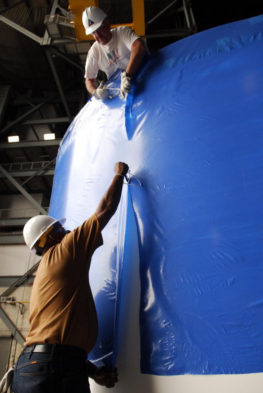 CAPE CANAVERAL, Fla. – Inside the Vehicle Assembly Building high bay 4 at NASA's Kennedy Space Center in Florida, workers from NASA's Glenn Research Center remove the blue shrink-wrapped covers on these Ares I-X upper stage simulator segments. The protective covers were used for shipping. The upper stage simulator will be used in the test flight identified as Ares I-X in 2009. The segments will simulate the mass and the outer mold line and will be more than 100 feet of the total vehicle height of 327 feet. The simulator comprises 11 segments that are approximately 18 feet in diameter. Most of the segments will be approximately 10 feet high, ranging in weight from 18,000 to 60,000 pounds, for a total of approximately 450,000 pounds. Photo credit: NASA/Troy Cryder