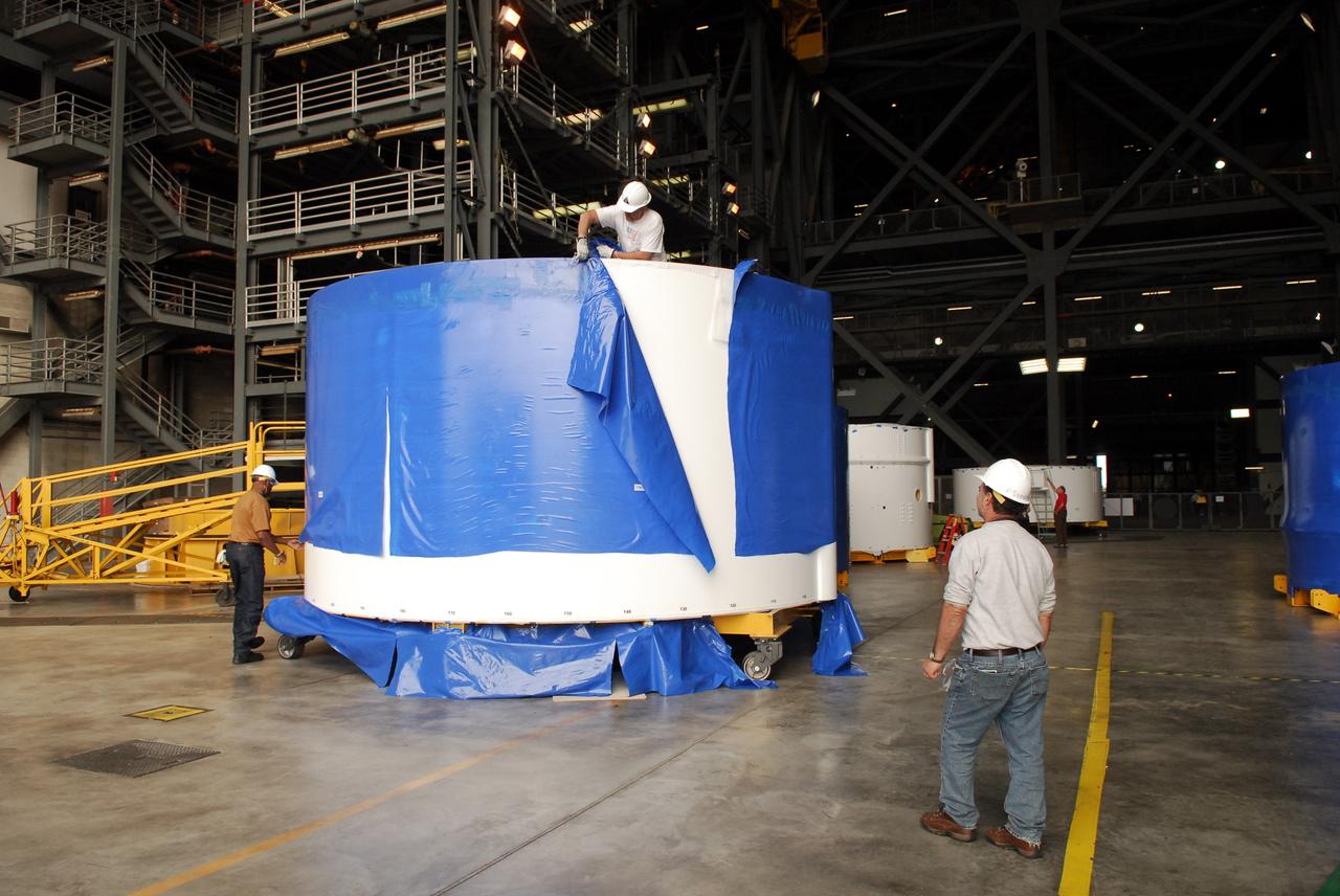 CAPE CANAVERAL, Fla. – Inside the Vehicle Assembly Building high bay 4 at NASA's Kennedy Space Center in Florida, workers from NASA's Glenn Research Center remove the blue shrink-wrapped covers on these Ares I-X upper stage simulator segments. The protective covers were used for shipping. The upper stage simulator will be used in the test flight identified as Ares I-X in 2009. The segments will simulate the mass and the outer mold line and will be more than 100 feet of the total vehicle height of 327 feet. The simulator comprises 11 segments that are approximately 18 feet in diameter. Most of the segments will be approximately 10 feet high, ranging in weight from 18,000 to 60,000 pounds, for a total of approximately 450,000 pounds. Photo credit: NASA/Troy Cryder