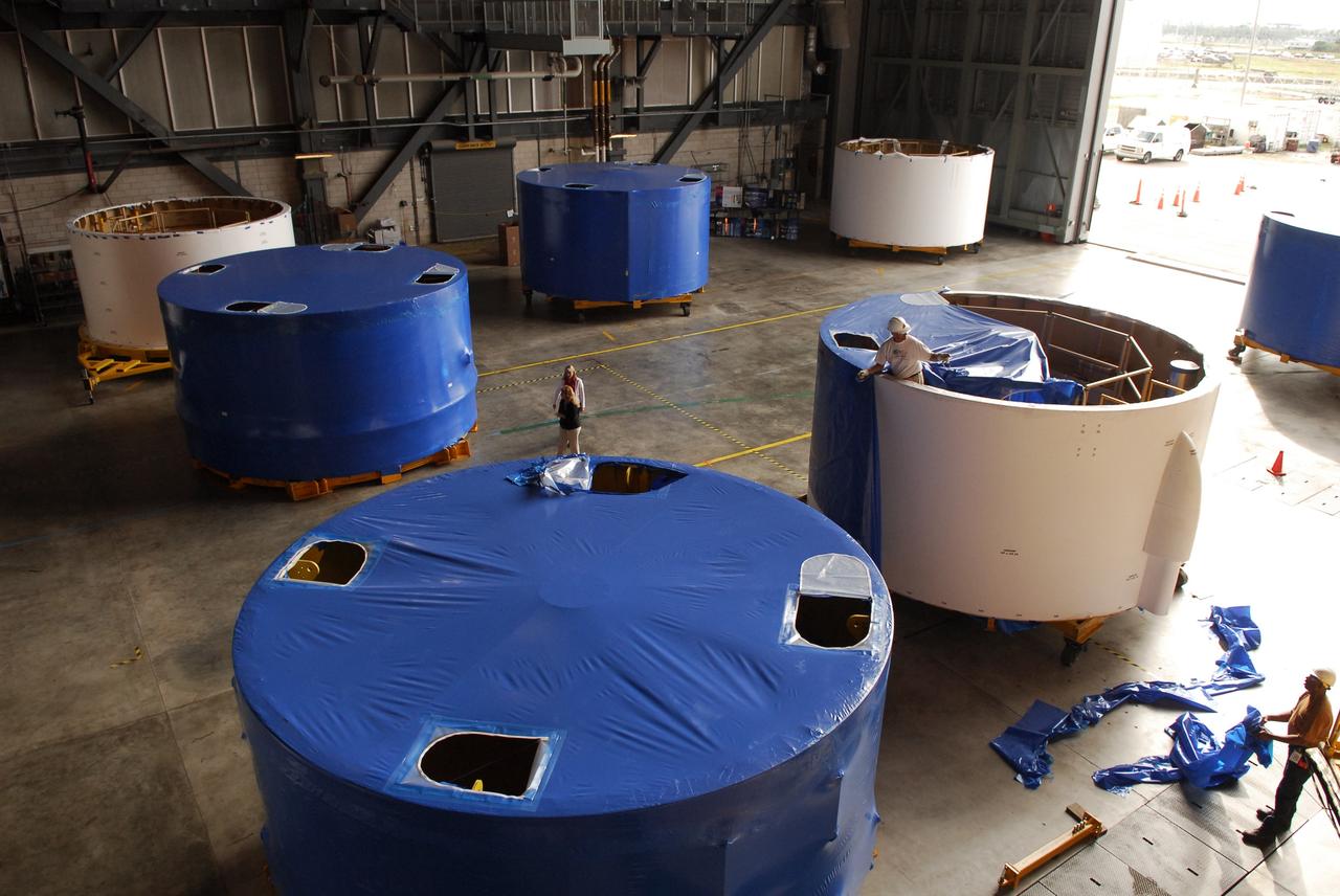 CAPE CANAVERAL, Fla. – Inside the Vehicle Assembly Building high bay 4 at NASA's Kennedy Space Center in Florida, workers from NASA's Glenn Research Center remove the blue shrink-wrapped covers on these Ares I-X upper stage simulator segments. The protective covers were used for shipping. The upper stage simulator will be used in the test flight identified as Ares I-X in 2009. The segments will simulate the mass and the outer mold line and will be more than 100 feet of the total vehicle height of 327 feet. The simulator comprises 11 segments that are approximately 18 feet in diameter. Most of the segments will be approximately 10 feet high, ranging in weight from 18,000 to 60,000 pounds, for a total of approximately 450,000 pounds. Photo credit: NASA/Troy Cryder