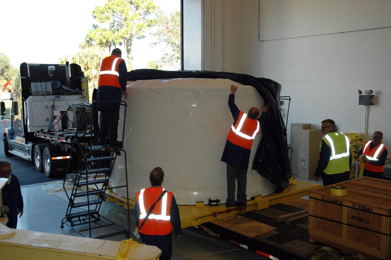 CAPE CANAVERAL, Fla. – Alliant Techsystems Inc. workers at Astrotech in Titusville, Fla., remove the protective outer shipping cover from the Ares I-X forward skirt after its arrival from Major Tool & Machine Inc. in Indiana. Major Tool is subcontractor to Ares I prime contractor Alliant Techsystems Inc., or ATK, in Utah. The forward skirt is the initial piece of first-stage hardware in preparation for the July 2009 test flight of the agency's next-generation spacecraft and launch vehicle system. Built entirely of armored steel, the 14,000-pound segment is seven feet tall and 12-1/4 feet wide. United Space Alliance, under a subcontract to ATK, will integrate and assemble the forward skirt components in the Assembly and Refurbishment Facility at NASA's Kennedy Space Center in Florida.. It will then be moved to the Vehicle Assembly Building high bay 3 for stacking operations. Photo credit: NASA/Tim Jacobs
