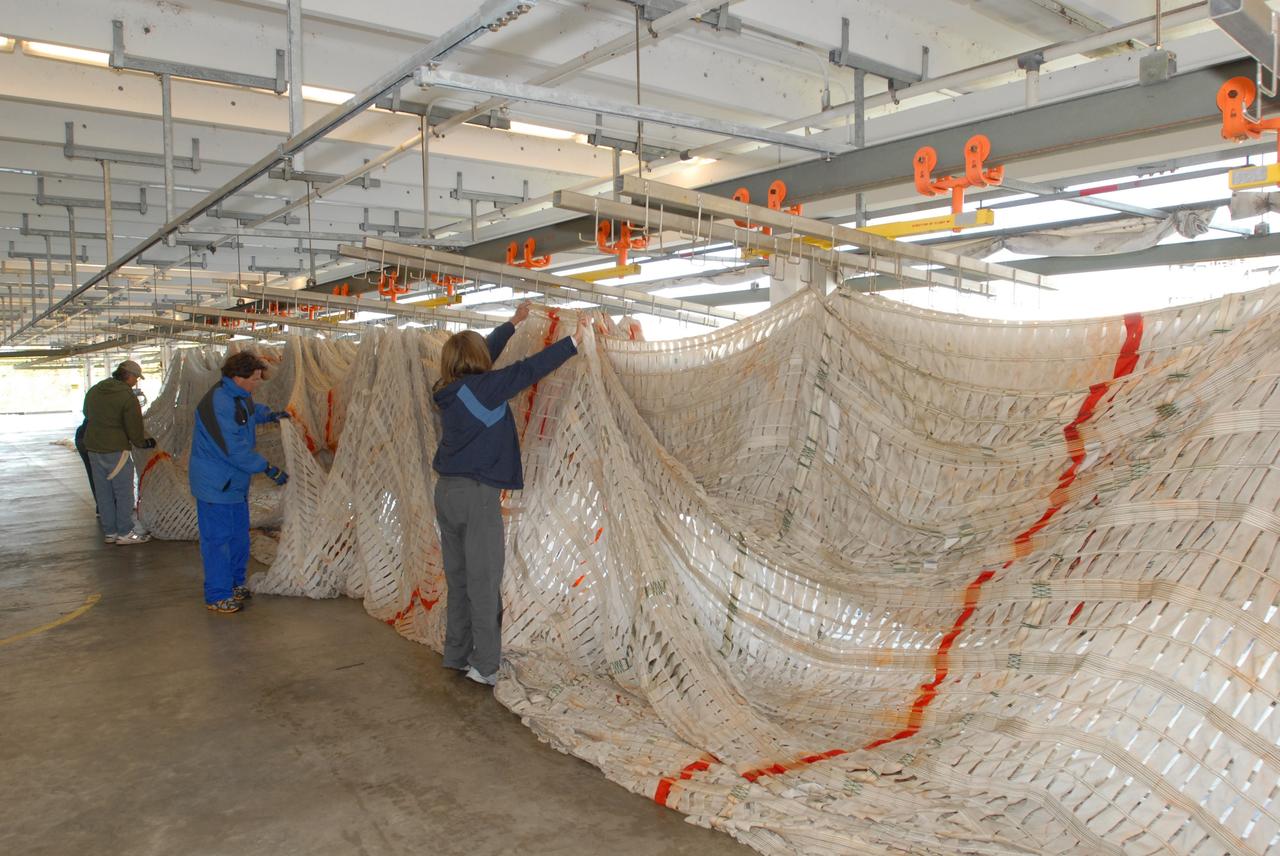 CAPE CANAVERAL, Fla. – At the Parachute Refurbishment Facility at NASA's Kennedy Space Center in Florida, workers begin hanging the parachutes recovered from sea after the launch of space shuttle Endeavour on the STS-126 mission onto a monorail system. The parachutes are used to slow the descent of the solid rocket boosters that are jettisoned during liftoff. The monorail will transport each parachute into a 30,000-gallon washer and a huge dryer heated with 140-degree air at 13,000 cubic feet per minute One pilot, one drogue and three main canopies per booster slow the booster’s fall from about 360 mph to 50 mph. After the chutes are cleaned and repaired, they must be carefully packed into their bags so they will deploy correctly the next time they are used. Photo credit: NASA/Jim Grossmann