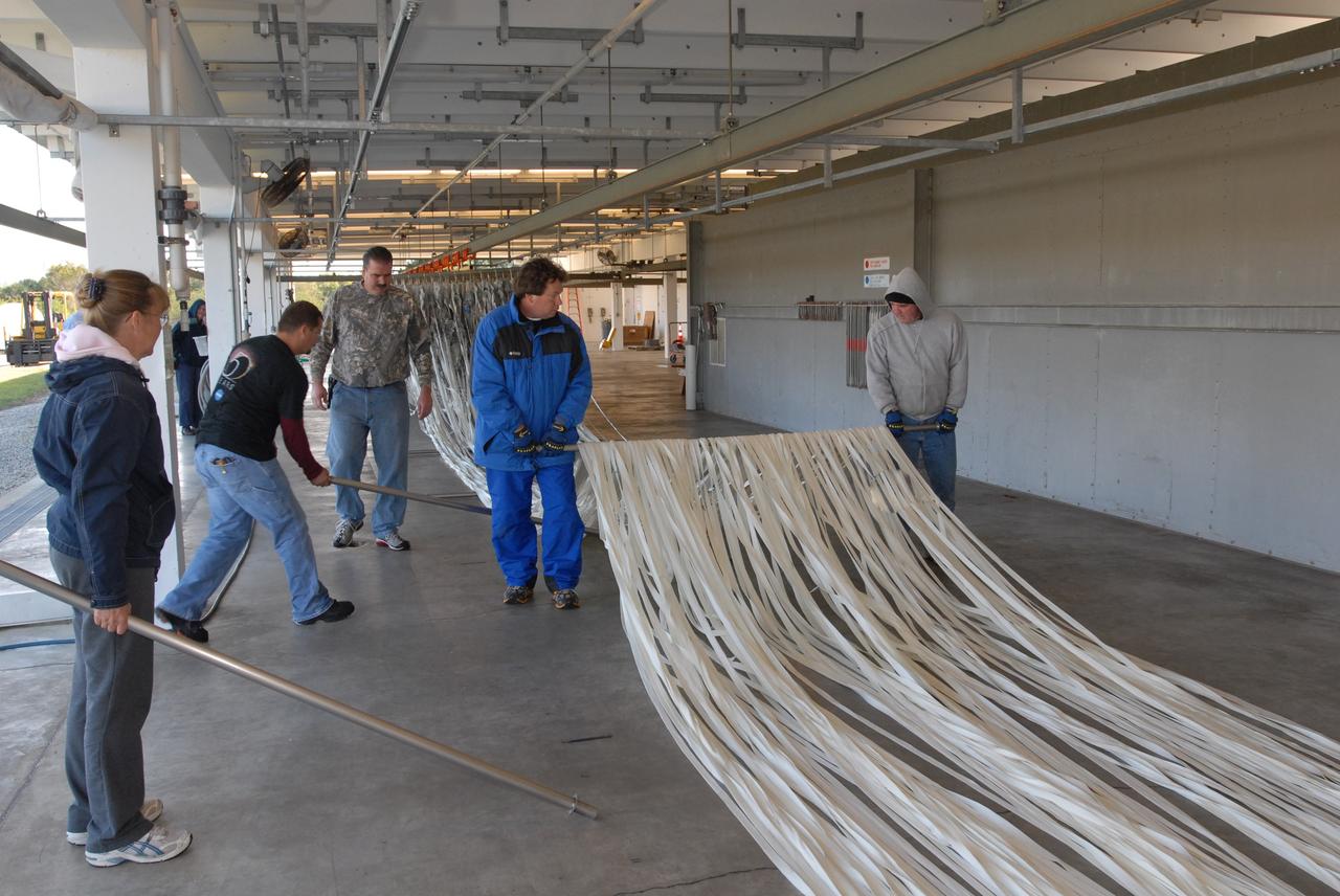 CAPE CANAVERAL, Fla. – At the Parachute Refurbishment Facility at NASA's Kennedy Space Center in Florida, workers place rods under the lines of the parachutes recovered from sea after the launch of space shuttle Endeavour on the STS-126 mission to hang them on a monorail system. Behind them, the parachutes are suspended from the monorail. The parachutes are used to slow the descent of the solid rocket boosters that are jettisoned during liftoff. The monorail will transport each parachute into a 30,000-gallon washer and a huge dryer heated with 140-degree air at 13,000 cubic feet per minute. One pilot, one drogue and three main canopies per booster slow the booster’s fall from about 360 mph to 50 mph. After the chutes are cleaned and repaired, they must be carefully packed into their bags so they will deploy correctly the next time they are used. Photo credit: NASA/Jim Grossmann