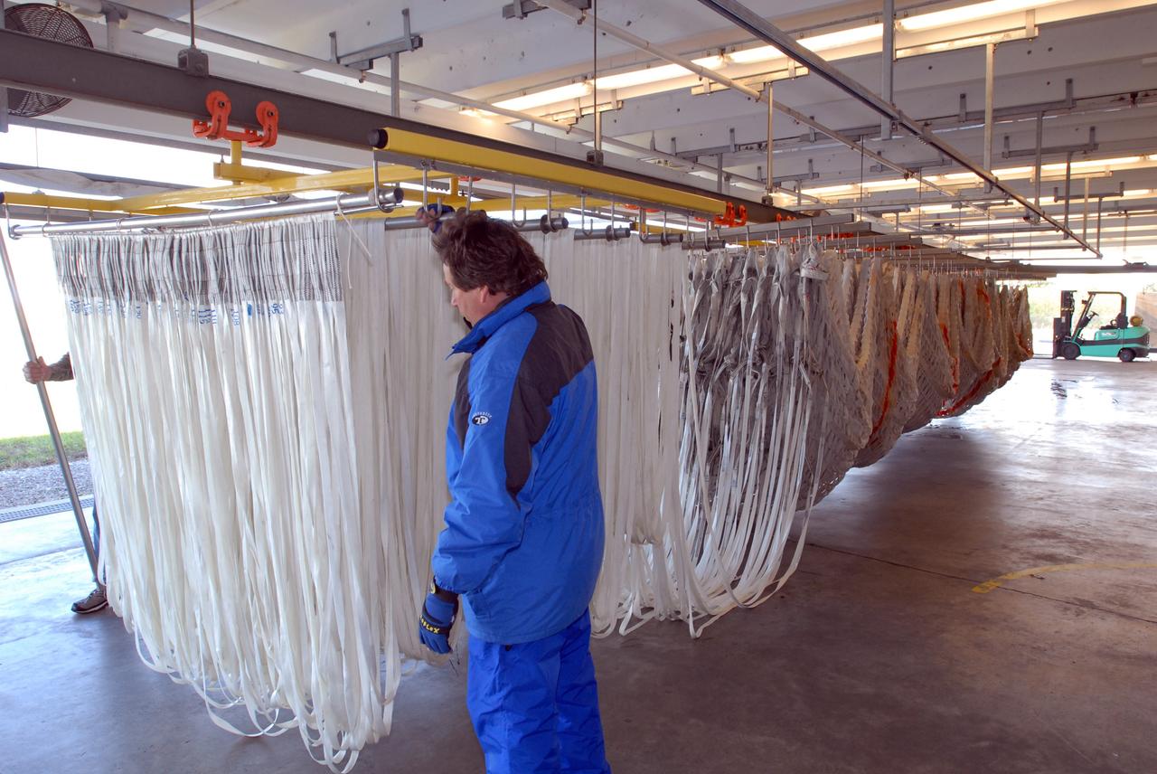CAPE CANAVERAL, Fla. – At the Parachute Refurbishment Facility at NASA's Kennedy Space Center in Florida, a worker checks the parachute lines suspended from the monorail system. The parachutes were recovered from sea after the launch of space shuttle Endeavour on the STS-126 mission The parachutes are used to slow the descent of the solid rocket boosters that are jettisoned during liftoff. The monorail will transport each parachute into a 30,000-gallon washer and a huge dryer heated with 140-degree air at 13,000 cubic feet per minute. One pilot, one drogue and three main canopies per booster slow the booster’s fall from about 360 mph to 50 mph. After the chutes are cleaned and repaired, they must be carefully packed into their bags so they will deploy correctly the next time they are used. Photo credit: NASA/Jim Grossmann