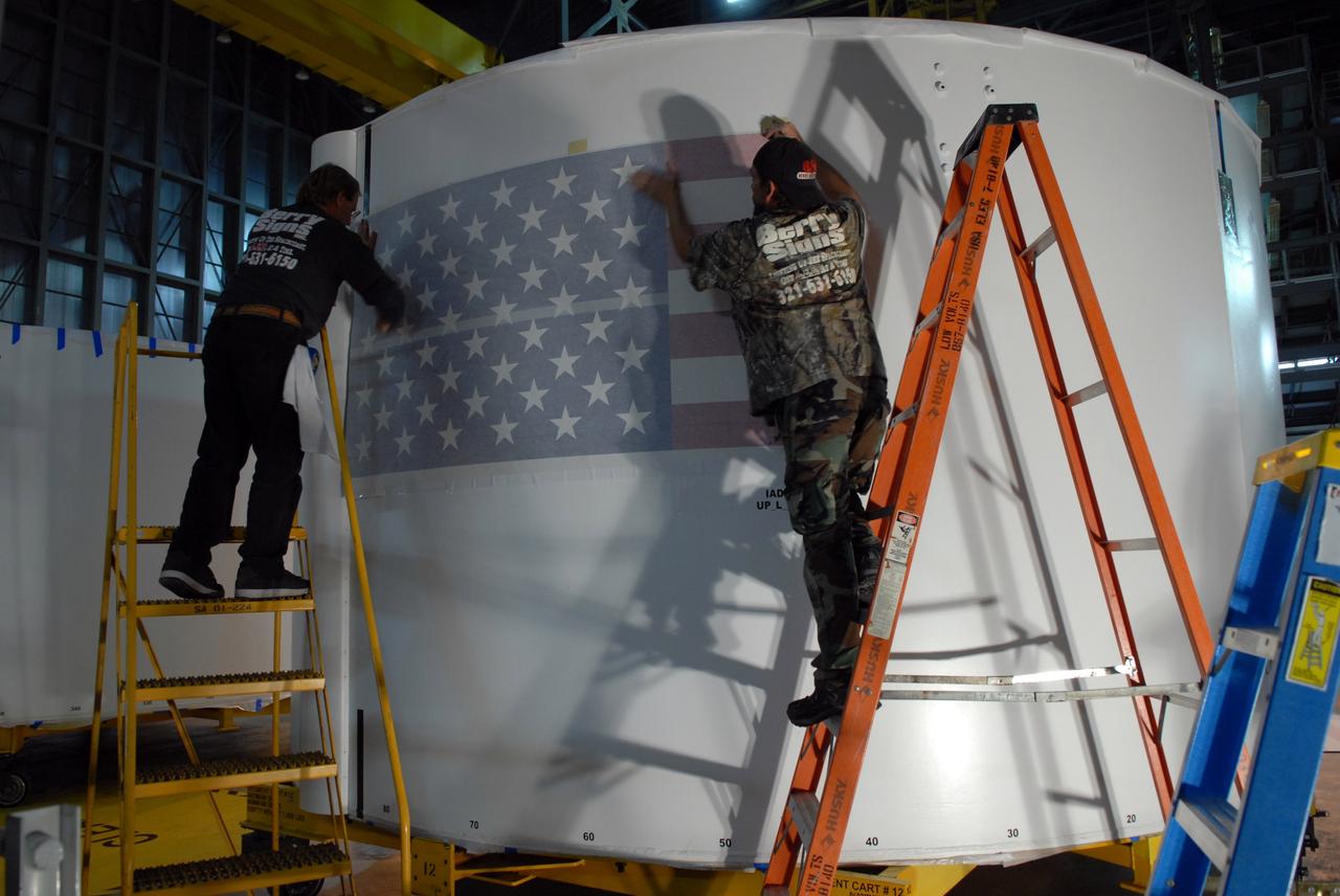 CAPE CANAVERAL, Fla. –   In the Vehicle Assembly Building high bay 4 at NASA's Kennedy Space Center in Florida, workers adhere a decal of the U.S. flag on one of the Ares I-X upper stage simulator segments. The upper stage simulator will be used in the test flight identified as Ares I-X in 2009.  Ares I-X is the test vehicle for the Ares I, which is part of the Constellation Program to return men to the moon and beyond.  Ares I is the essential core of a safe, reliable, cost-effective space transportation system that eventually will carry crewed missions back to the moon, on to Mars and out into the solar system. Ares I may also use its 25-ton payload capacity to deliver resources and supplies to the International Space Station, or to "park" payloads in orbit for retrieval by other spacecraft bound for the moon or other destinations.  Photo credit: NASA/Jack Pfaller