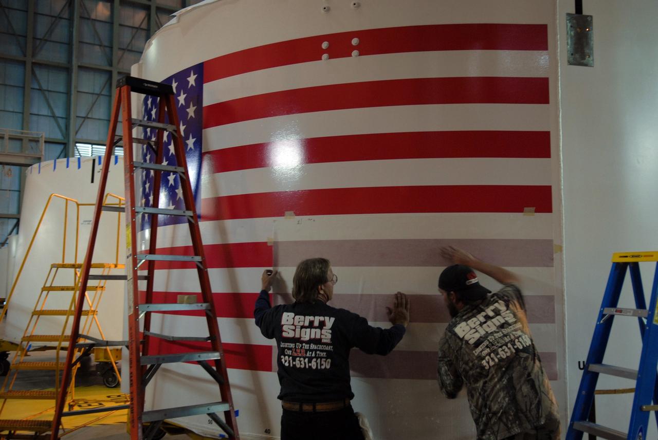 CAPE CANAVERAL, Fla. –   In the Vehicle Assembly Building high bay 4 at NASA's Kennedy Space Center in Florida, workers remove the final cover from the U.S. flag decal affixed to one of the Ares I-X upper stage simulator segments. The upper stage simulator will be used in the test flight identified as Ares I-X in 2009.  Ares I-X is the test vehicle for the Ares I, which is part of the Constellation Program to return men to the moon and beyond.  Ares I is the essential core of a safe, reliable, cost-effective space transportation system that eventually will carry crewed missions back to the moon, on to Mars and out into the solar system. Ares I may also use its 25-ton payload capacity to deliver resources and supplies to the International Space Station, or to "park" payloads in orbit for retrieval by other spacecraft bound for the moon or other destinations.  Photo credit: NASA/Jack Pfaller