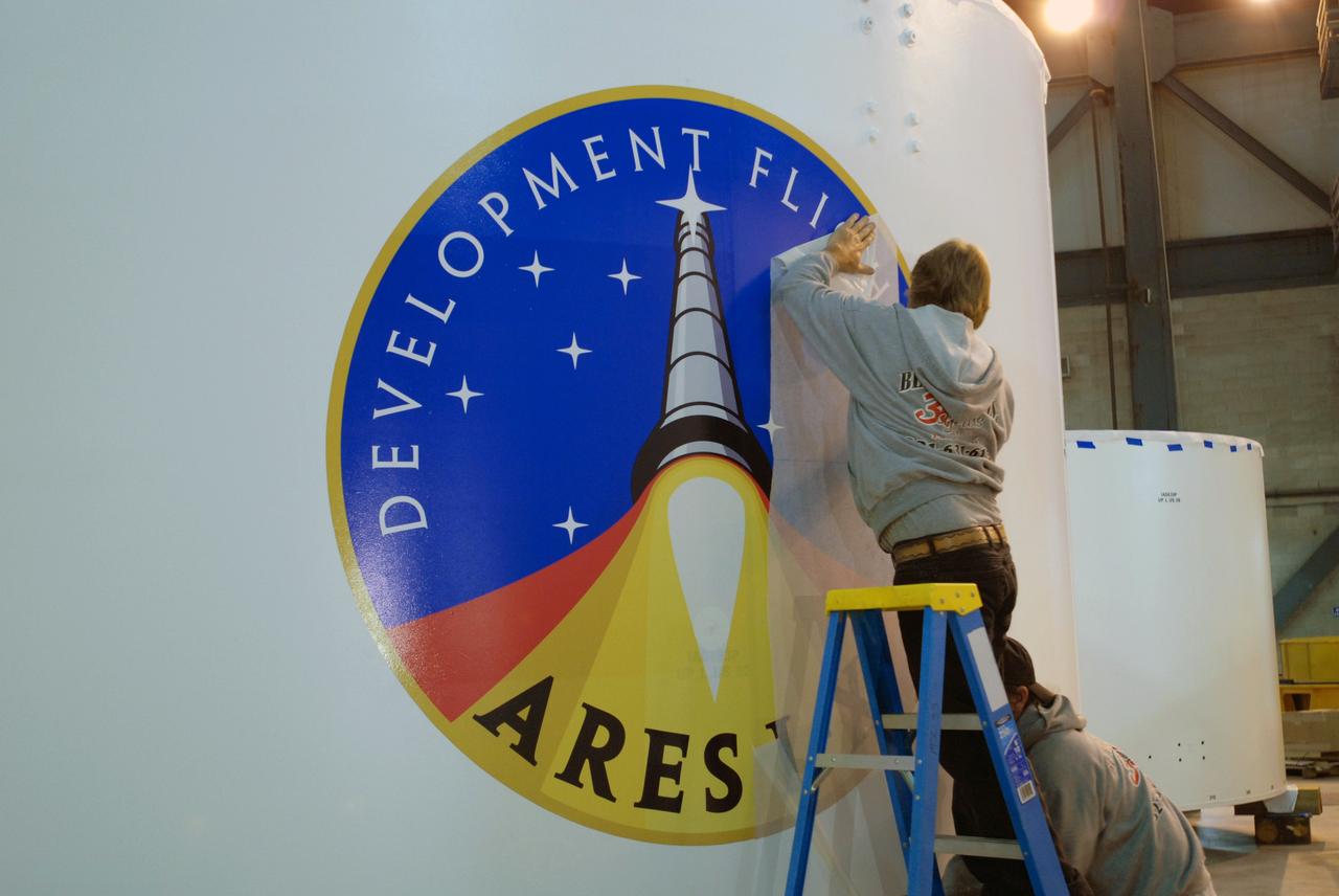 CAPE CANAVERAL, Fla. – In the Vehicle Assembly Building high bay 4 at NASA's Kennedy Space Center in Florida, a worker removes the last piece of cover from the final Ares I-X logo on one of the Ares I-X upper stage simulator segments.  The decal identifies the Ares I-X as a development test flight, which is targeted to launch in 2009. Ares I is the essential core of a safe, reliable, cost-effective space transportation system that eventually will carry crewed missions back to the moon, on to Mars and out into the solar system. Ares I may also use its 25-ton payload capacity to deliver resources and supplies to the International Space Station, or to "park" payloads in orbit for retrieval by other spacecraft bound for the moon or other destinations.    Photo credit: NASA/Jim Grossmann