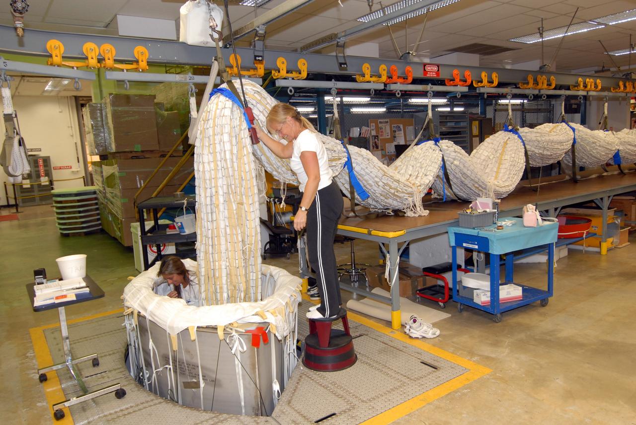 CAPE CANAVERAL, Fla. - In the Parachute Refurbishment Facility at NASA's Kennedy Space Center, United Space Alliance senior aero composite technicians Dior Hubel (kneeling) and Marcia Jones-Clark pack a main parachute slated for use on the Ares I-X test flight. The launch is targeted for July 2009 from Kennedy’s Launch Pad 39B and will provide an early opportunity to test and prove hardware, facilities and ground operations associated with the Ares I rocket. The Ares I-X rocket is a combination of existing and simulator hardware that will resemble the Ares I crew launch vehicle in size, shape and weight. It will provide valuable data to guide the final design of the Ares I, which will launch astronauts in the Orion crew exploration vehicle. The test flight also will bring NASA one step closer to its exploration goals of returning humans to the moon for sustained exploration of the lunar surface and missions to destinations beyond. Photo credit: NASA/Jack Pfaller