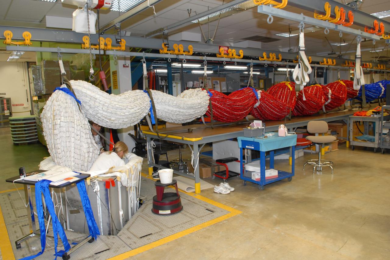 CAPE CANAVERAL, Fla. - In the Parachute Refurbishment Facility at NASA's Kennedy Space Center, United Space Alliance senior aero composite technicians Dior Hubel (behind parachute) and Marcia Jones-Clark pack a colorful main parachute slated for use on the Ares I-X test flight. The new parachutes are red, white and blue. The launch is targeted for July 2009 from Kennedy's Launch Pad 39B and will provide an early opportunity to test and prove hardware, facilities and ground operations associated with the Ares I rocket. The Ares I-X rocket is a combination of existing and simulator hardware that will resemble the Ares I crew launch vehicle in size, shape and weight. It will provide valuable data to guide the final design of the Ares I, which will launch astronauts in the Orion crew exploration vehicle. The test flight also will bring NASA one step closer to its exploration goals of returning humans to the moon for sustained exploration of the lunar surface and missions to destinations beyond. Photo credit: NASA/Jack Pfaller