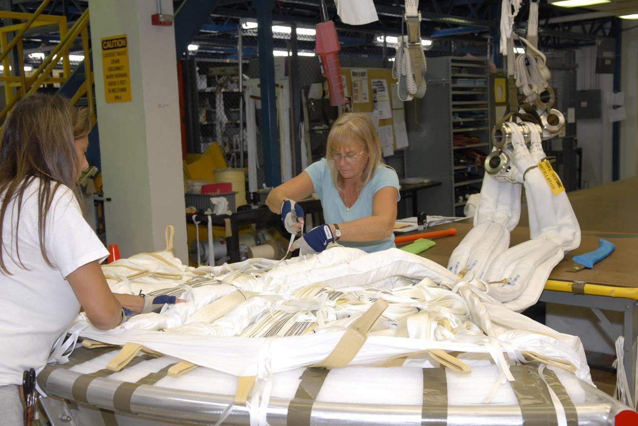 CAPE CANAVERAL, Fla. -- In the Parachute Refurbishment Facility at NASA's Kennedy Space Center in Florida, workers straighten the straps of the parachutes they are packing that will be used in the Ares I-X development flight in July 2009. The first stage of the new Ares I rocket and Orion spacecraft will use parachutes to return to Earth. Ares I-X is the test vehicle for the Ares I, which is part of the Constellation Program to return men to the moon and beyond. Ares I is the essential core of a safe, reliable, cost-effective space transportation system that eventually will carry crewed missions back to the moon, on to Mars and out into the solar system. Ares I may also use its 25-ton payload capacity to deliver resources and supplies to the International Space Station, or to "park" payloads in orbit for retrieval by other spacecraft bound for the moon or other destinations. Photo credit: NASA/Jack Pfaller
