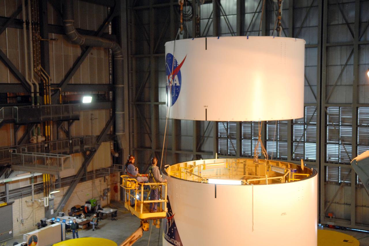 CAPE CANAVERAL, Fla. --  In high bay 4 of the Vehicle Assembly Building at NASA's Kennedy Space Center in Florida, a crane lowers segment 5 of the Ares I-X upper stage simulator segments toward segment 4, at top of the tall stack below. The upper stage simulator comprises 11 segments, each approximately 18 feet in diameter, that will be used in the test flight known as Ares I-X in 2009.  The simulator segments will simulate the mass and the outer mold line.  The upper stage accounts for nearly one-quarter of the total height of the Ares I.  It will take the Ares I on the second phase of its journey from Earth, providing the guidance, navigation and control needed for the second phase of the Ares I ascent flight.   Photo credit: NASA/Troy Cryder
