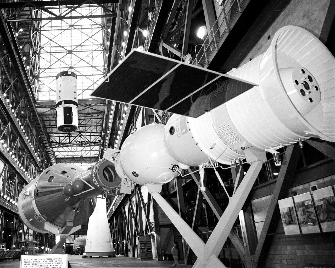 CAPE CANAVERAL, Fla. – Model of docked Apollo and Soyuz spacecraft in the foreground and skylight in the Vehicle Assembly Building high bay frame the second stage of the Saturn 1B booster that will launch the United States ASTP mission as a crane raises it prior to its mating with the Saturn 1B first stage.  Mating of the Saturn 1B first and second stages was completed this morning.  The U. S. ASTP launch with mission commander Thomas Stafford, command module pilot Vance Brand and docking module pilot Donald Slayton is scheduled at 3:50 p.m. EDT July 15.      The first international crewed spaceflight was a joint U.S.-U.S.S.R. rendezvous and docking mission.  The Apollo-Soyuz Test Project, or ASTP, took its name from the spacecraft employed: the American Apollo and the Soviet Soyuz.  The three-man Apollo crew lifted off from Kennedy Space Center aboard a Saturn IB rocket on July 15, 1975, to link up with the Soyuz that had launched a few hours earlier.  A cylindrical docking module served as an airlock between the two spacecraft for transfer of the crew members.  Photo credit: NASA