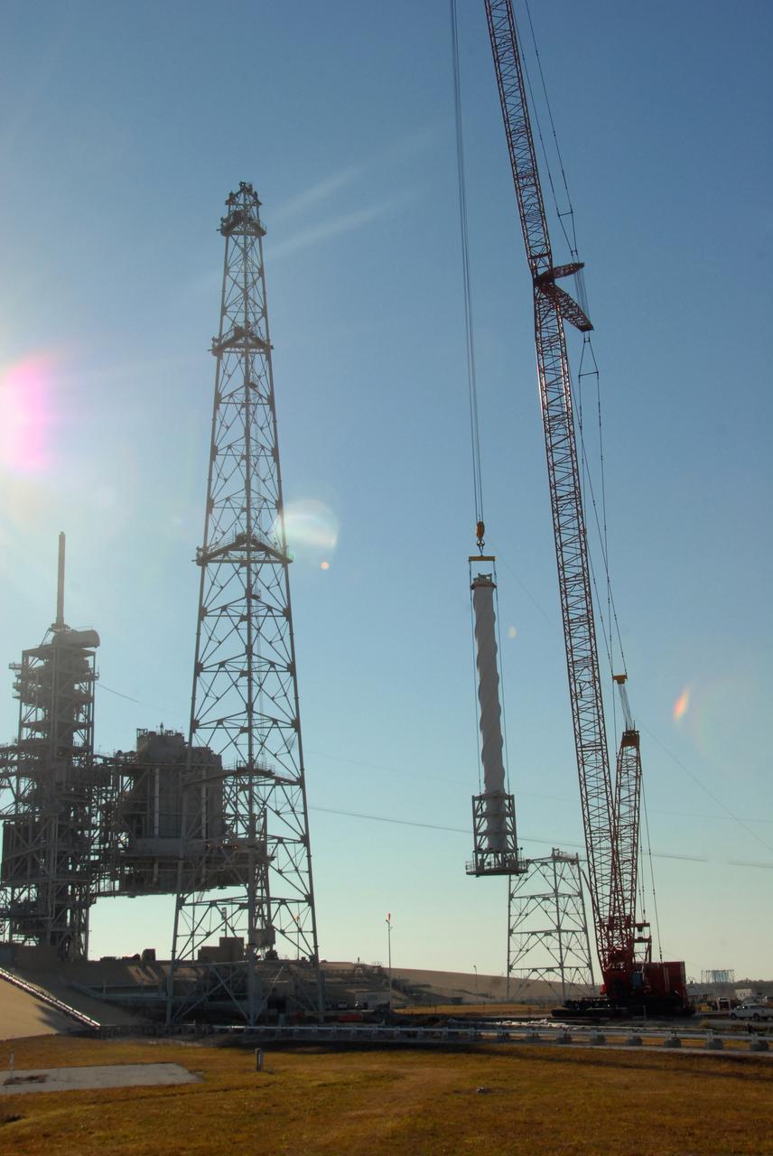 CAPE CANAVERAL, Fla. –  On Launch Pad 39B at NASA's Kennedy Space Center in Florida, a crane begins lifting a 100-foot fiberglass lightning mast to place it on top of one of the 500-foot towers being constructed for the Constellation Program and Ares/Orion launches. This improved lightning protection system allows for the taller height of the Ares I rocket compared to the space shuttle.  Pad 39B will be the site of the first Ares vehicle launch, including the Ares I-X test flight that is targeted for July 2009.