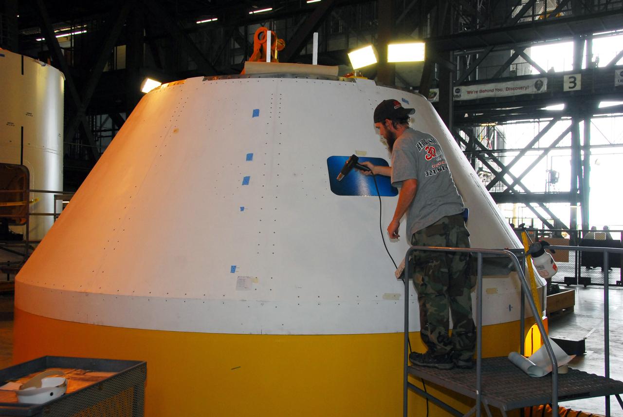 CAPE CANAVERAL, Fla. –   In high bay 4 of the Vehicle Assembly Building at NASA's Kennedy Space Center, a worker applies a window decal on the Ares I-X mock-up crew module.   Ares I-X is the test flight for the Ares I.   The I-X flight will provide NASA an early opportunity to test and prove hardware, facilities and ground operations associated with Ares I. The launch of full-scale Ares I-X, targeted for July 2009, will be the first in a series of unpiloted rocket launches from Kennedy. When fully developed, the 16-foot diameter crew module will furnish living space and reentry protection for the astronauts.  Photo credit: NASA/Tim Jacobs