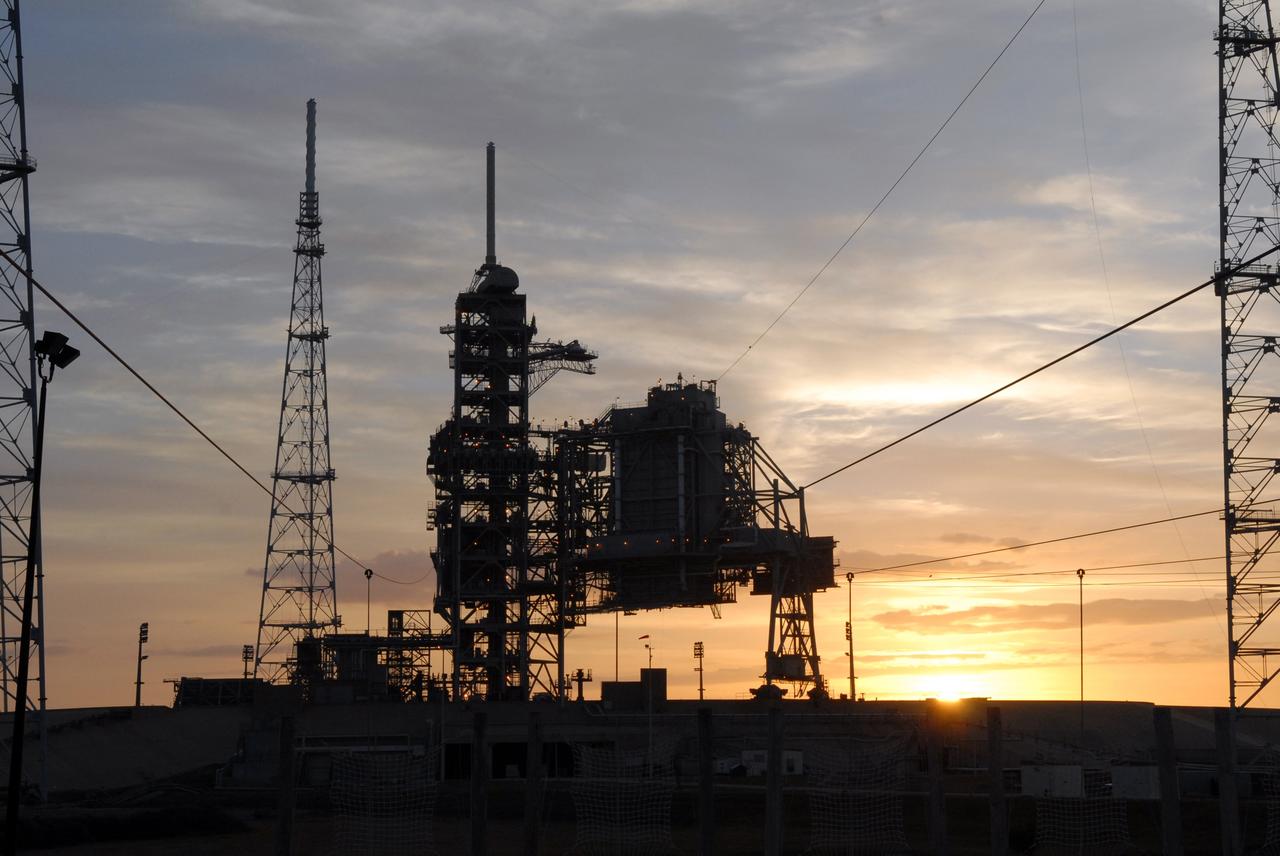 CAPE CANAVERAL, Fla. – The faint sunrise sky over NASA's Kennedy Space Center casts the newly erected lightning towers on Launch Pad 39B in silhouette.  They surround the fixed and rotating service structures at center that have served the Space Shuttle Program.  The new lightning protection system is being built for the Constellation Program and Ares/Orion launches.  Each of the towers is 500 feet tall with an additional 100-foot fiberglass mast atop supporting a wire catenary system.  This improved lightning protection system allows for the taller height of the Ares I rocket compared to the space shuttle.  Pad 39B will be the site of the first Ares vehicle launch, including the Ares I-X test flight that is targeted for July 2009. Photo credit: NASA/Jack Pfaller