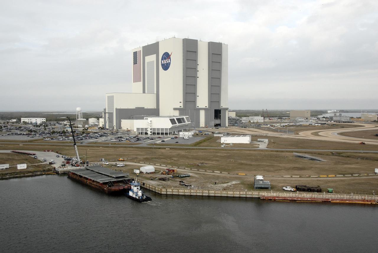 CAPE CANAVERAL, Fla. – An aerial view of the Launch Complex 39 Area NASA's Kennedy Space Center in Florida shows the 525-foot-tall Vehicle Assembly Building looming over the landscape. In the foreground is the turn basin, where a barge holds trestles and girders for the new mobile launcher. The new launcher will be the base for the Constellation Program's Ares rockets to launch the Orion crew exploration vehicle and the cargo vehicle. The base is being made lighter than space shuttle mobile launcher platforms so the crawler-transporter can pick up the added load of the 345-foot tower and taller rocket. When the structural portion of the new mobile launcher is complete, umbilicals, access arms, communications equipment and command/control equipment will be installed. Photo credit: NASA/Kim Shiflett