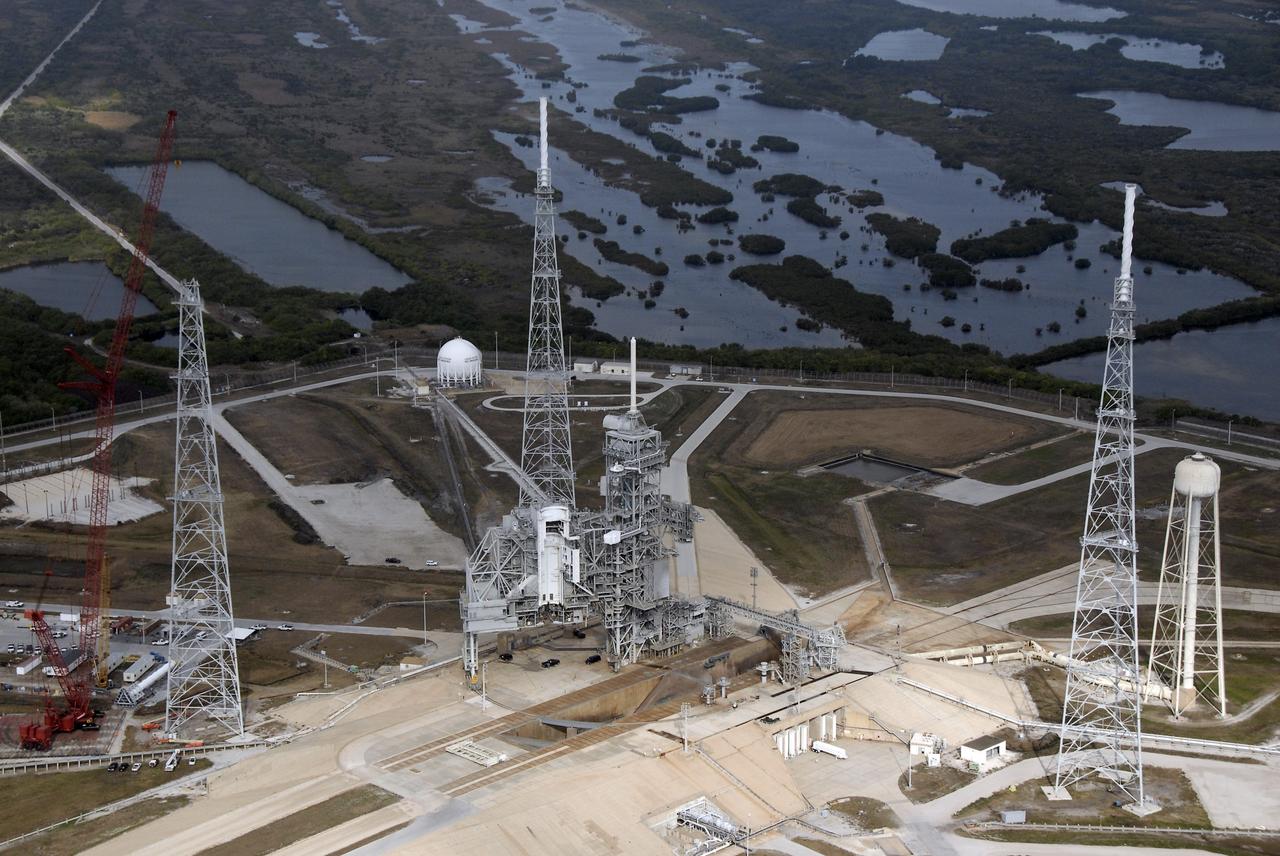 CAPE CANAVERAL, Fla. – An aerial view of the newly erected lightning towers on Launch Pad 39B at NASA's Kennedy Space Center. The two towers at center and right contain the lightning mast on top; the one at left does not. At center are the fixed and rotating service structures that have served the Space Shuttle Program. In the foreground is the tower that holds 300,000 gallons of water used for sound suppression during a shuttle liftoff. The new lightning protection system is being built for the Constellation Program and Ares/Orion launches. Each of the towers is 500 feet tall with an additional 100-foot fiberglass mast atop supporting a wire catenary system. This improved lightning protection system allows for the taller height of the Ares I rocket compared to the space shuttle. Pad 39B will be the site of the first Ares rocket launch, including the Ares I-X test flight that is targeted for July 2009. Photo credit: NASA/Kim Shiflett