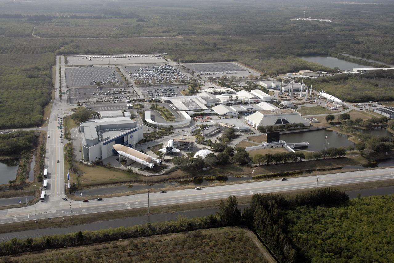 CAPE CANAVERAL, Fla. – An aerial view shows the entire Kennedy Space Center Visitor Complex in Florida. In the foreground at left are a full-size orbiter replica, the "Explorer," which allows guests to picture more clearly what it's like to live and work in space, as well as full-size, genuine solid rocket boosters and an external fuel tank (foreground, left). On the right at center is the rocket garden, which features eight authentic rockets from the past, including a Mercury-Atlas rocket similar to the one used to launch John Glenn into space in 1962 and climb-in Mercury, Gemini and Apollo capsule rep¬licas. Photo credit: NASA/Kim Shiflett