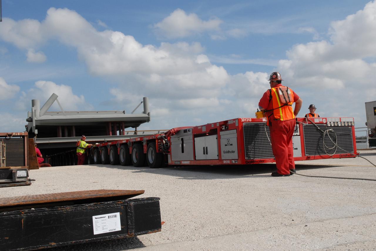 CAPE CANAVERAL, Fla. – At the turn basin in the Launch Complex 39 Area of NASA's Kennedy Space Center in Florida, a long transporter moves closer to the barge for offloading of the girder for a new mobile launcher. The new mobile launcher will be the base for the Ares rockets to launch the Orion crew exploration vehicle and the cargo vehicle. The base is being made lighter than space shuttle mobile launcher platforms so the crawler-transporter can pick up the added load of the 345-foot tower and taller rocket. When the structural portion of the new mobile launcher is complete, umbilicals, access arms, communications equipment and command/control equipment will be installed. Photo credit: NASA/Jack Pfaller